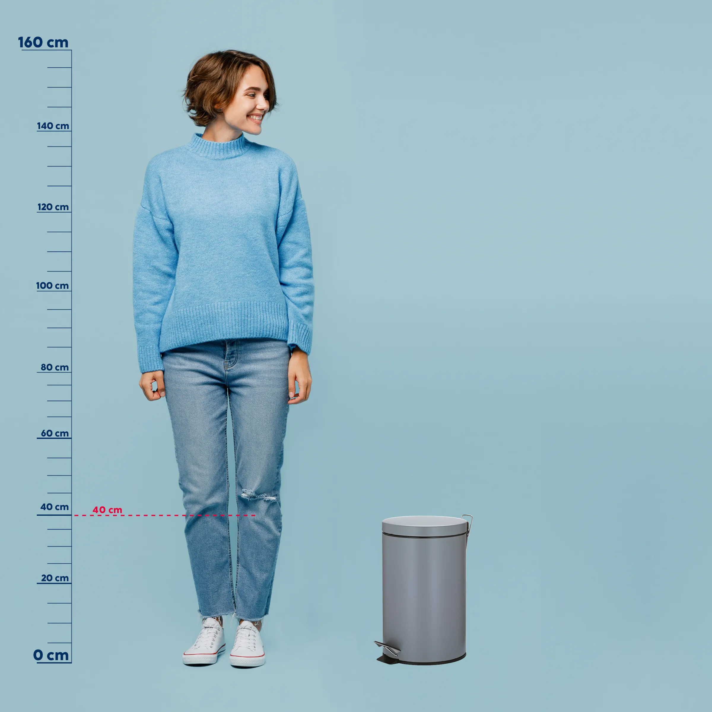 Mülleimer Größenvergleich – Abfallbehälter Produktfoto Frau mit braunem Haar in blauem Rollkragenpullover und zerrissener Jeans neben grauem Mülleimer vor blauem Hintergrund
