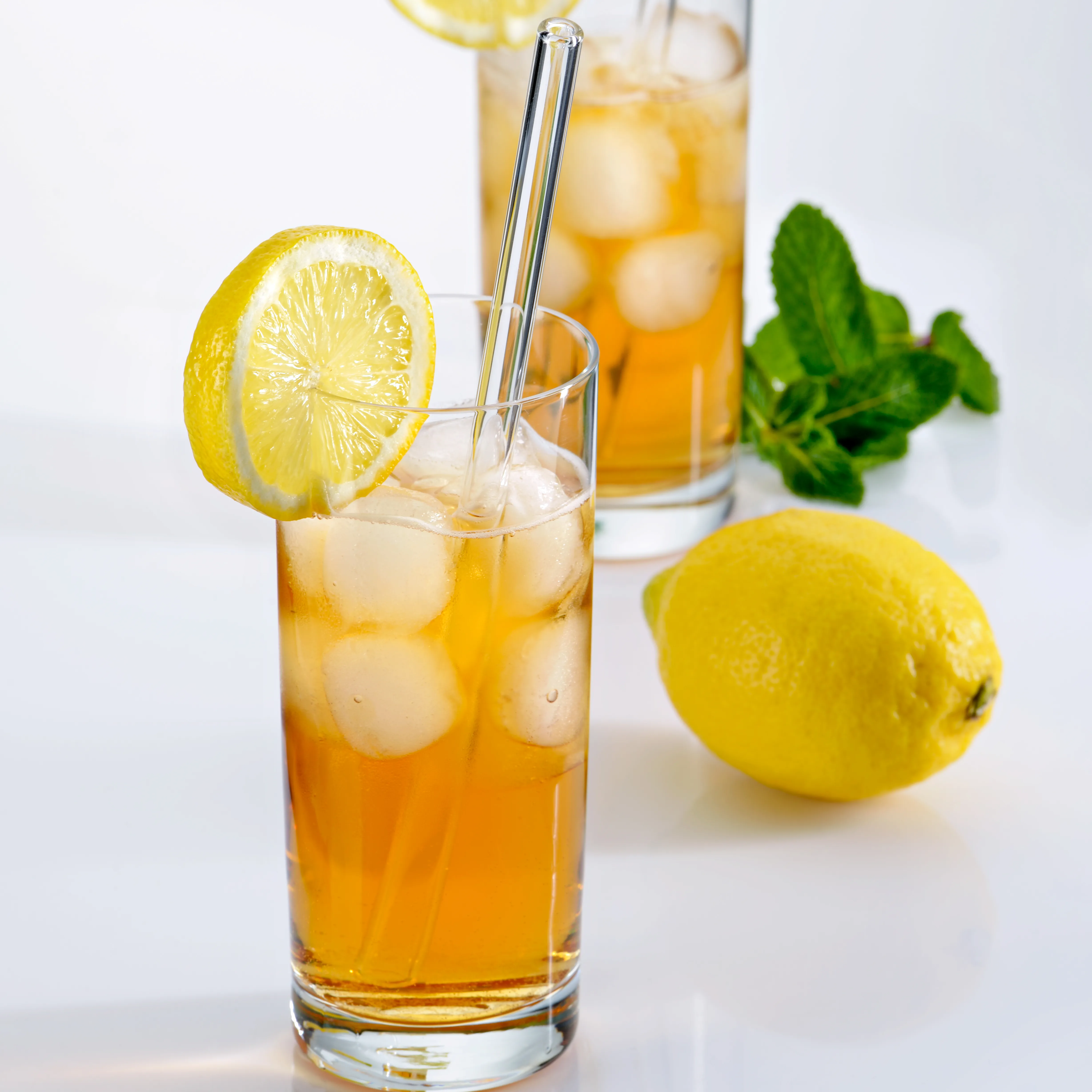 Erfrischender Zitronencocktail mit Eiswürfeln und Minze Glas mit orangefarbenem Getränk, Eiswürfeln, Zitronenscheibe und Strohhalm neben frischen Zitronen und Minzblättern