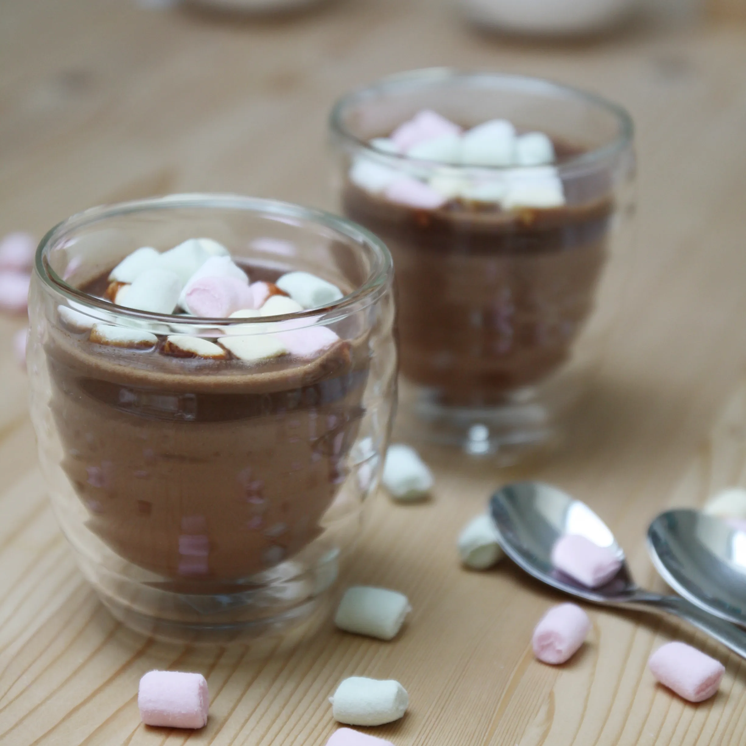 Heiße Schokolade mit Marshmallows - Wintergetränk im Glas Zwei Gläser heiße Schokolade mit rosa und weißen Marshmallows, daneben liegen Löffel und weitere Marshmallows