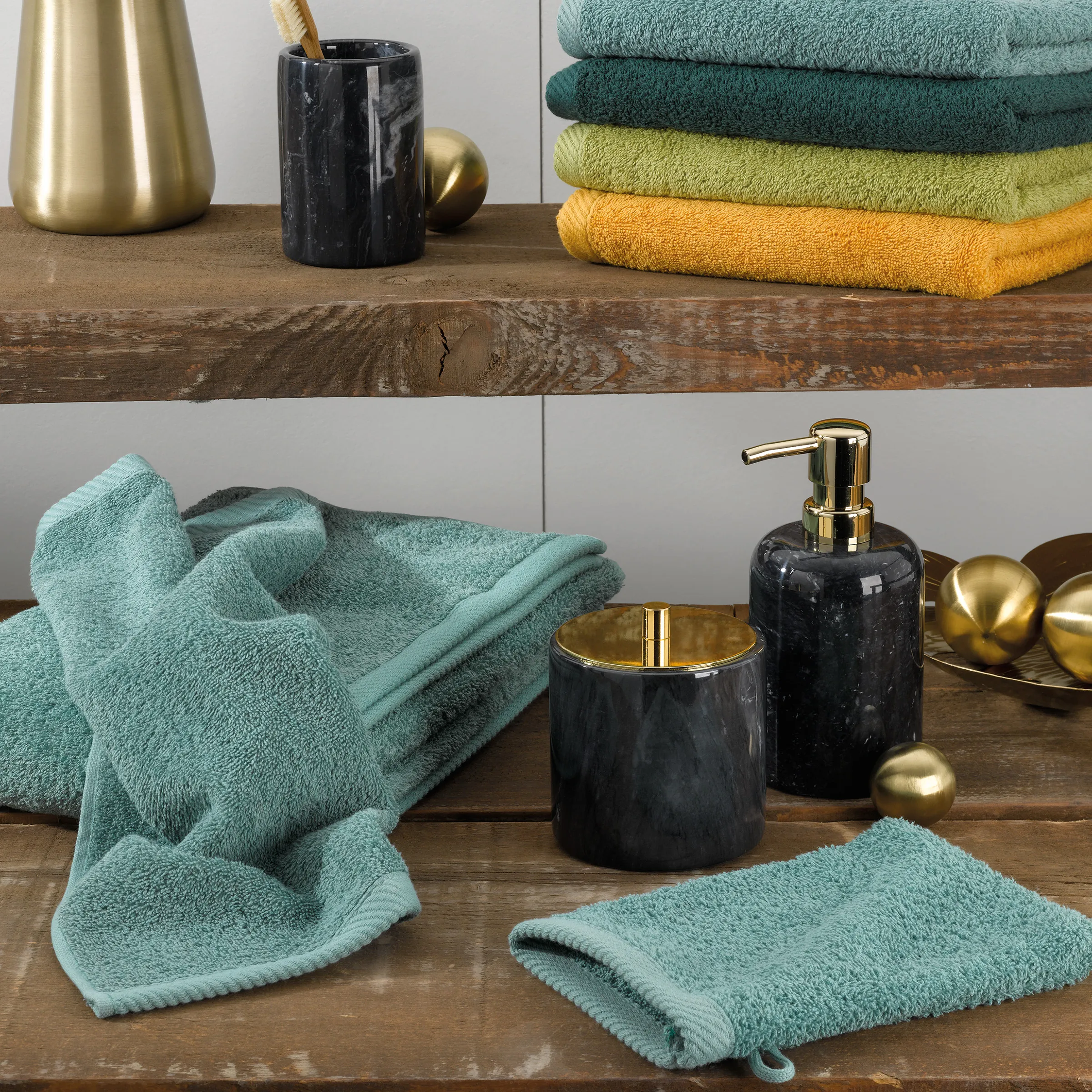 Badezimmer-Set mit türkisen Handtüchern, schwarzen Marmor-Behältern mit goldenen Applikationen und dekorativen Kugeln auf Holzregalen.