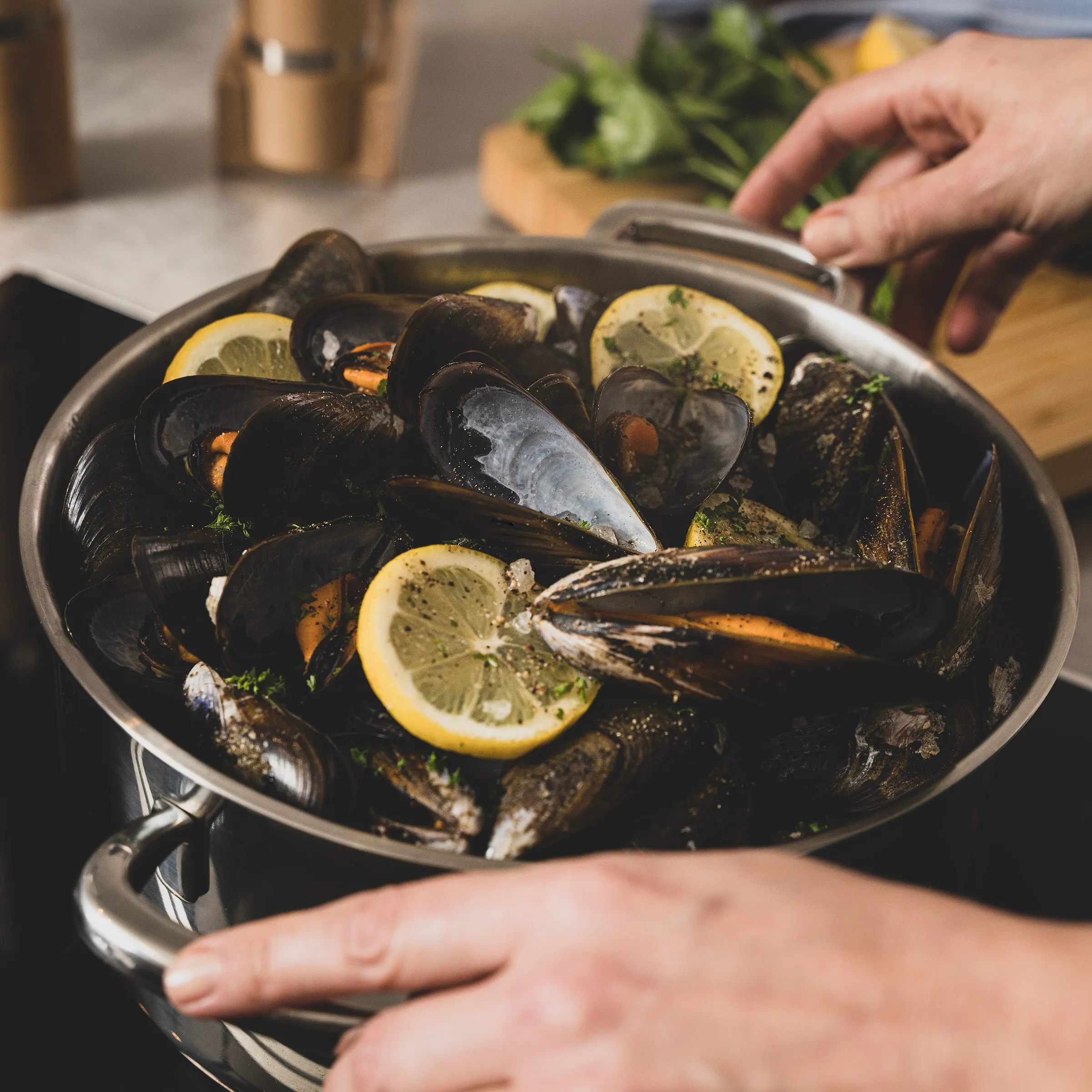Muscheln Rezept mit Zitrone und Kräutern - einfache Zubereitung Schwarze Muscheln mit Zitronenscheiben und frischen Kräutern in einer Pfanne, die von Händen gehalten wird.