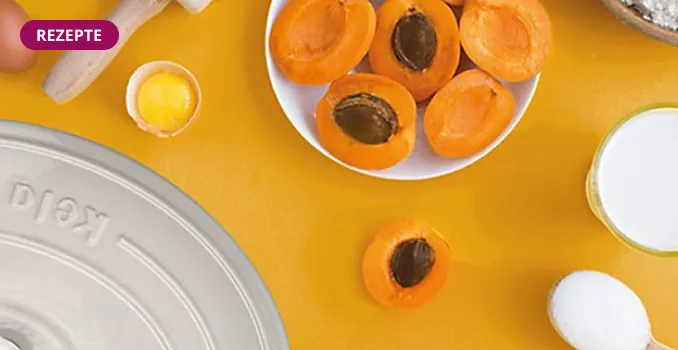 Kochzutaten auf gelbem Hintergrund: frische Aprikosen in Schüssel, Eier, Butter und weitere Backzutaten für Rezept