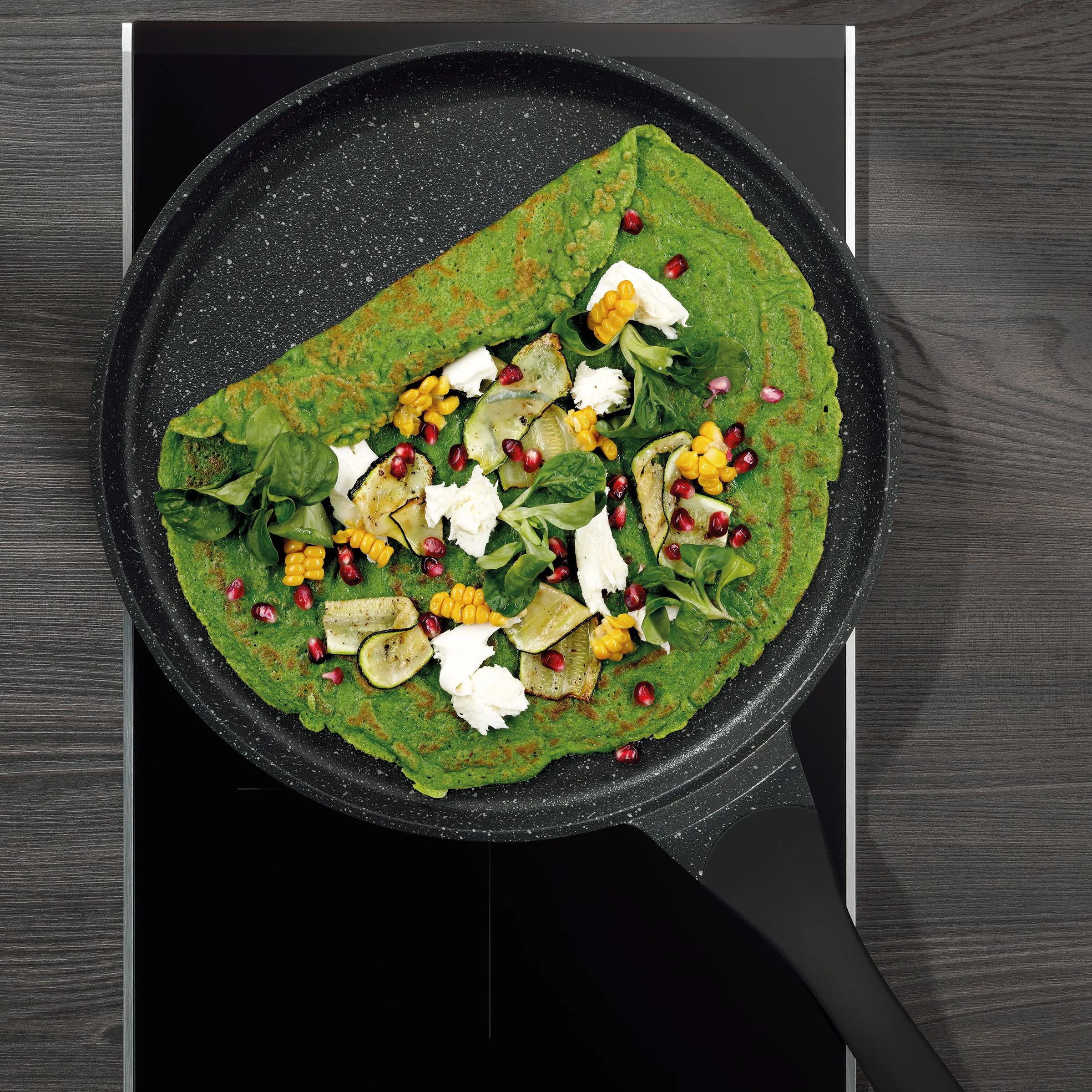 Grüner Gemüse-Pfannkuchen mit Ziegenkäse und Granatapfel - Gesundes Rezept Grüner Pfannkuchen mit Ziegenkäse, gegrilltem Gemüse, Mais und Granatapfelkernen in schwarzer Pfanne