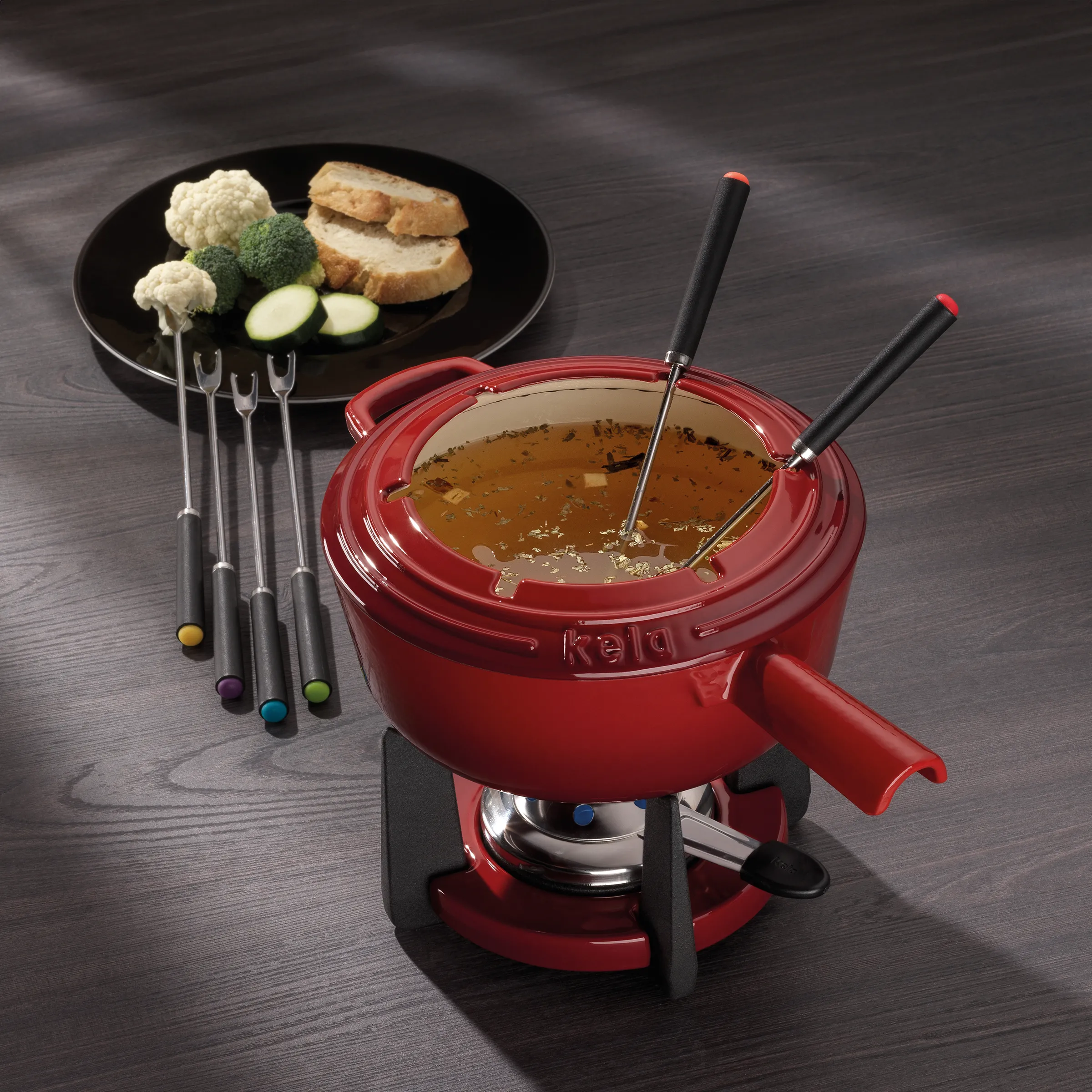 Käla Fondue-Set rot mit Gabeln - Fleischfondue Käsefondue Brühe Rotes Käla Fondue-Set mit Brühe, Gabeln und Teller mit Fleisch und Gemüse auf dunklem Holztisch