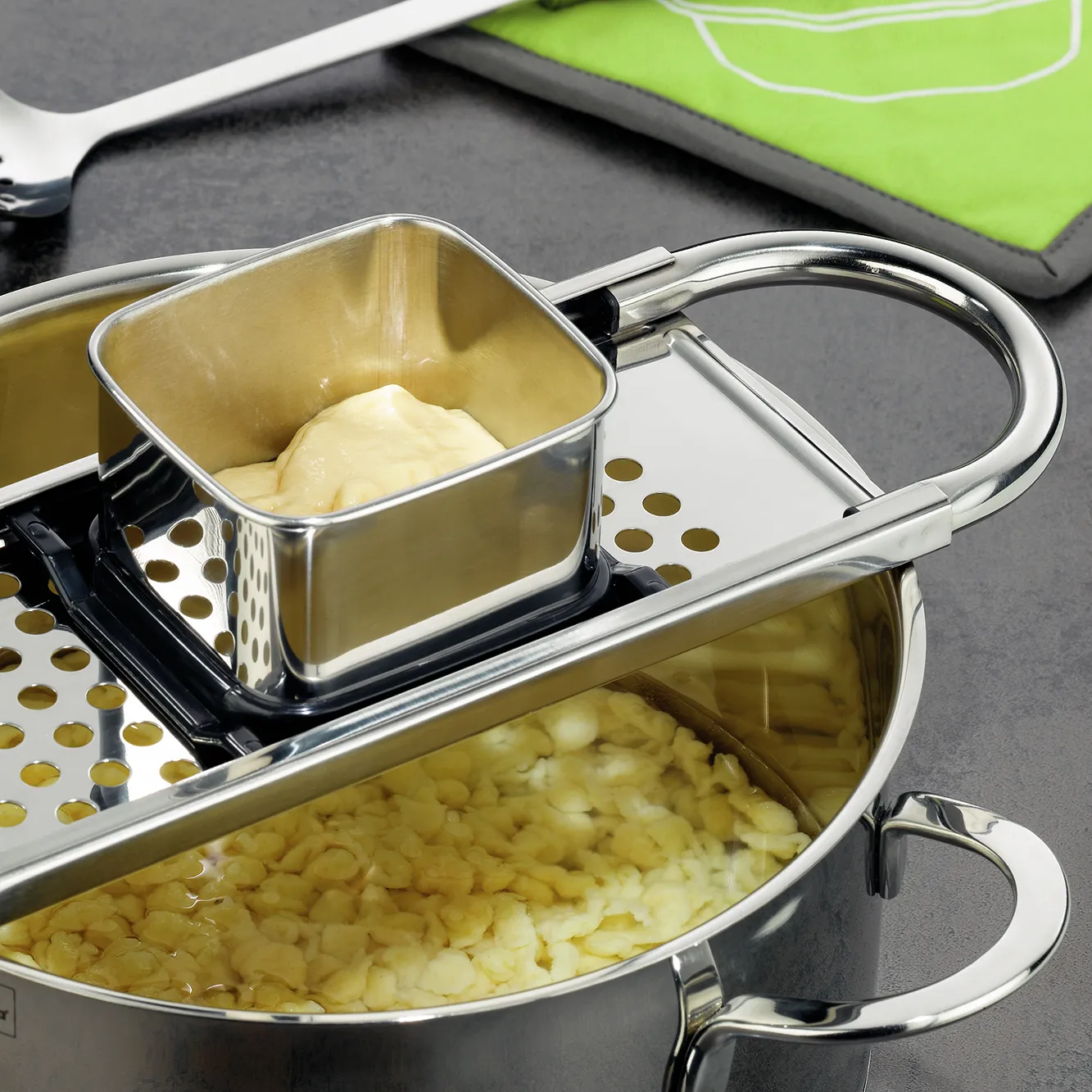 Kochtopf-Set mit Pasta-Einsatz und Siebeinsatz für Nudeln Edelstahl-Kochtopf mit Pasta-Einsatz, gefüllt mit Nudeln und Butter auf grauer Arbeitsfläche