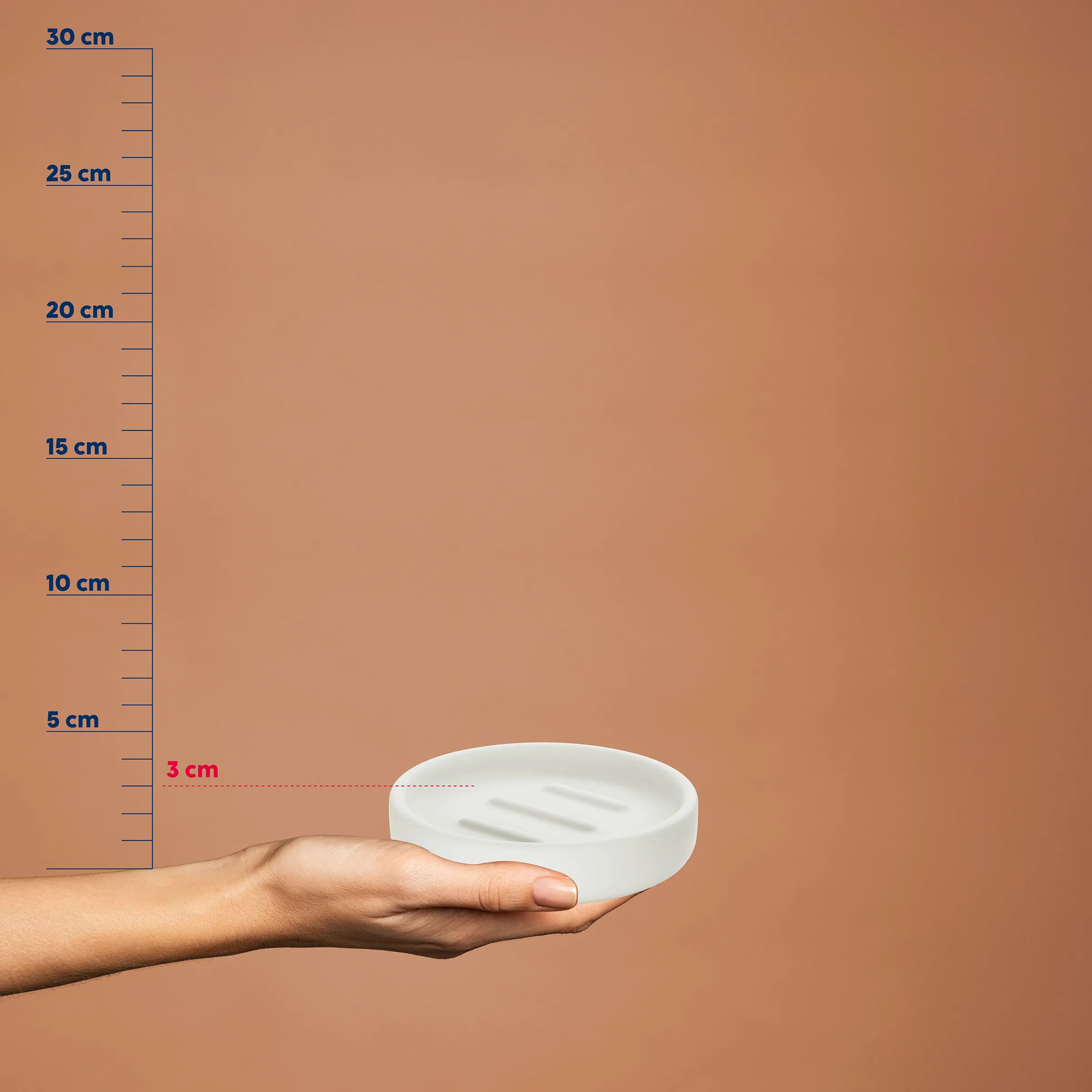 Seifenschale mit Ablauf – Größenvergleich mit Maßstab Hand hält weiße Seifenschale mit Ablauflöchern vor Maßstab, Höhe 3 cm