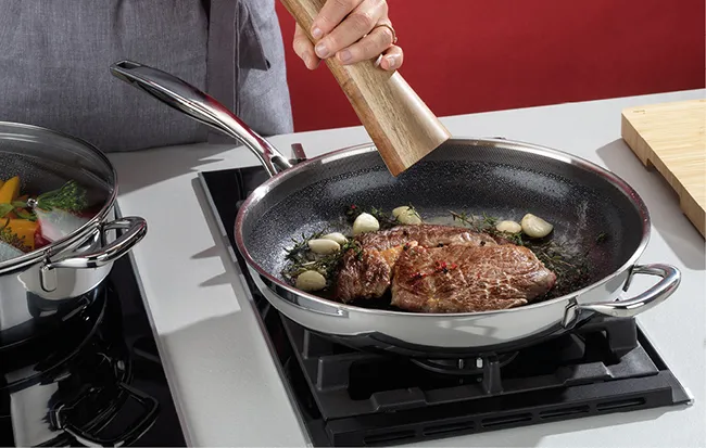 Person brät Fleisch in einer Pfanne auf Induktionskochfeld, daneben steht ein Topf mit Gemüse