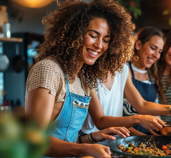 Gemeinsam Kochen: Fröhliche Frauen bereiten gesundes Essen in der Küche zu Zwei lächelnde Frauen in Schürzen kochen gemeinsam in moderner Küche, Fokus auf Gemüsepfanne