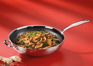 Edelstahl-Bratpfanne mit Nudelpfanne - Asiatisches Pfannengericht mit Gemüse Edelstahl-Bratpfanne mit asiatischem Nudelgericht, Gemüse und Garnelen auf rotem Hintergrund