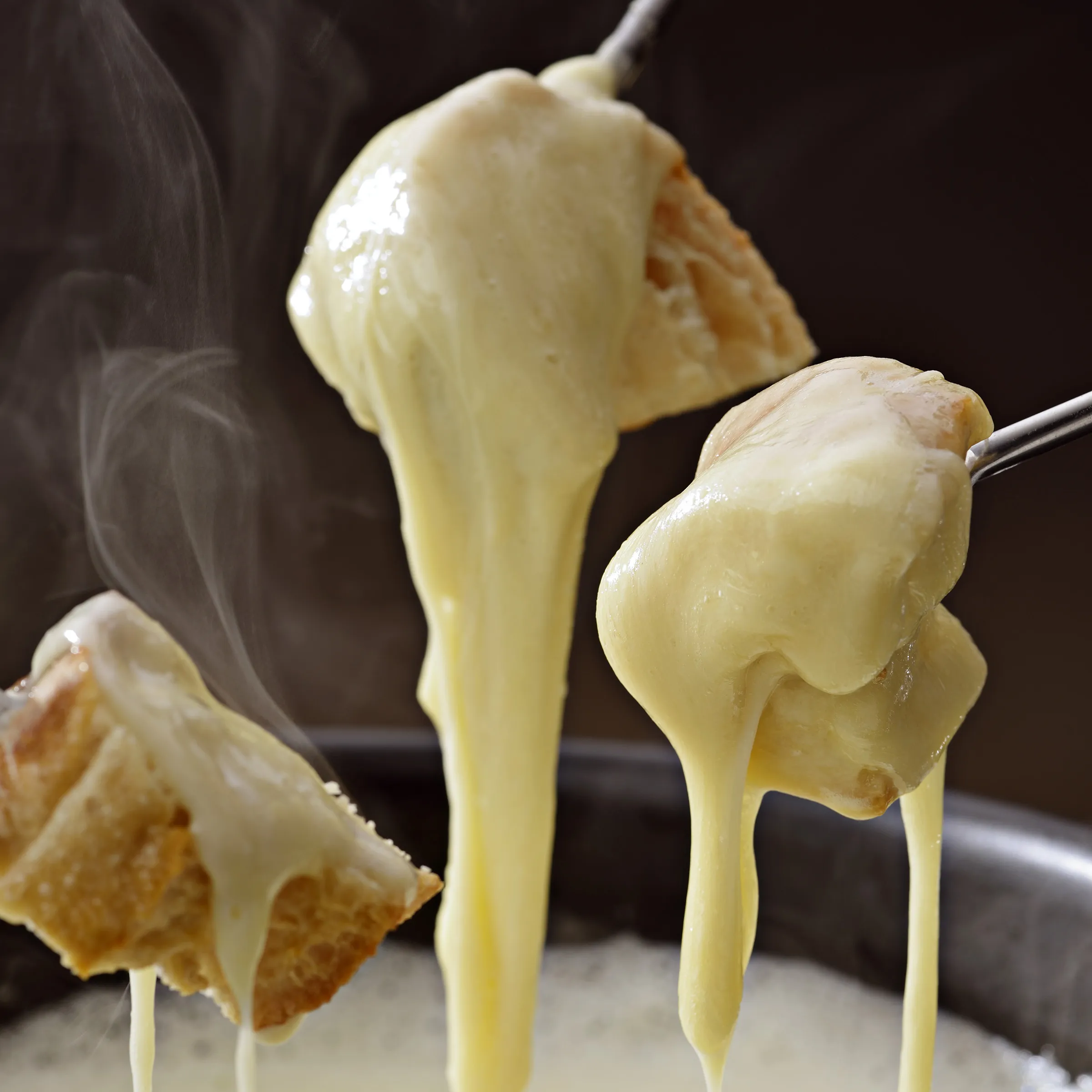 Geschmolzener Raclette-Käse zieht lange Fäden von Brotspießen über einem Raclette-Grill