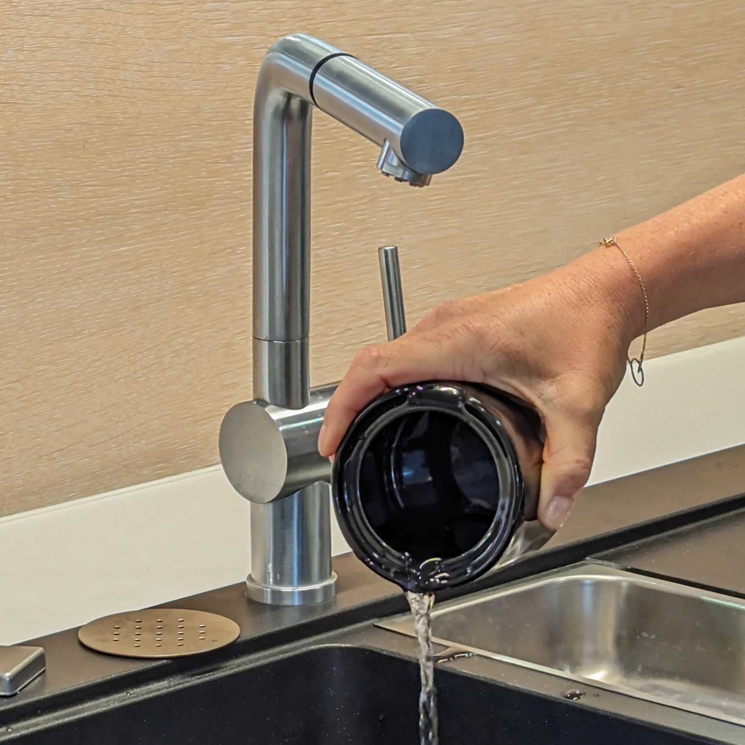 Moderne Küchenarmatur mit ausziehbarer Brause - Edelstahl Wasserhahn Hand füllt schwarze Trinkflasche mit Wasser an moderner Edelstahl-Küchenarmatur mit ausziehbarer Brause