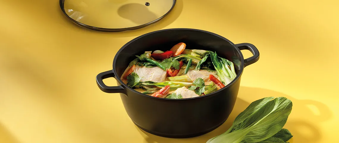 Kochtopf mit Hähnchen-Gemüse-Eintopf Rezept Schwarzer Topf mit Deckel auf gelbem Hintergrund, gefüllt mit Hühnerbrühe, Hähnchenbrust, grünen Bohnen und Paprika