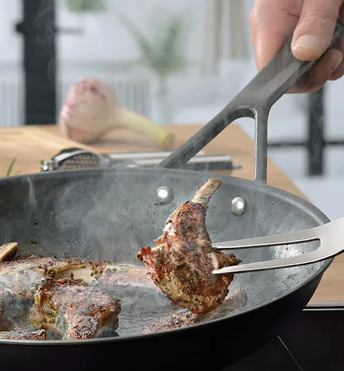 Lammkoteletts braten mit Grillzange in Grillpfanne - Küchenzubehör Hand hält Grillzange und wendet Lammkotelett in grauer Grillpfanne auf Induktionskochfeld
