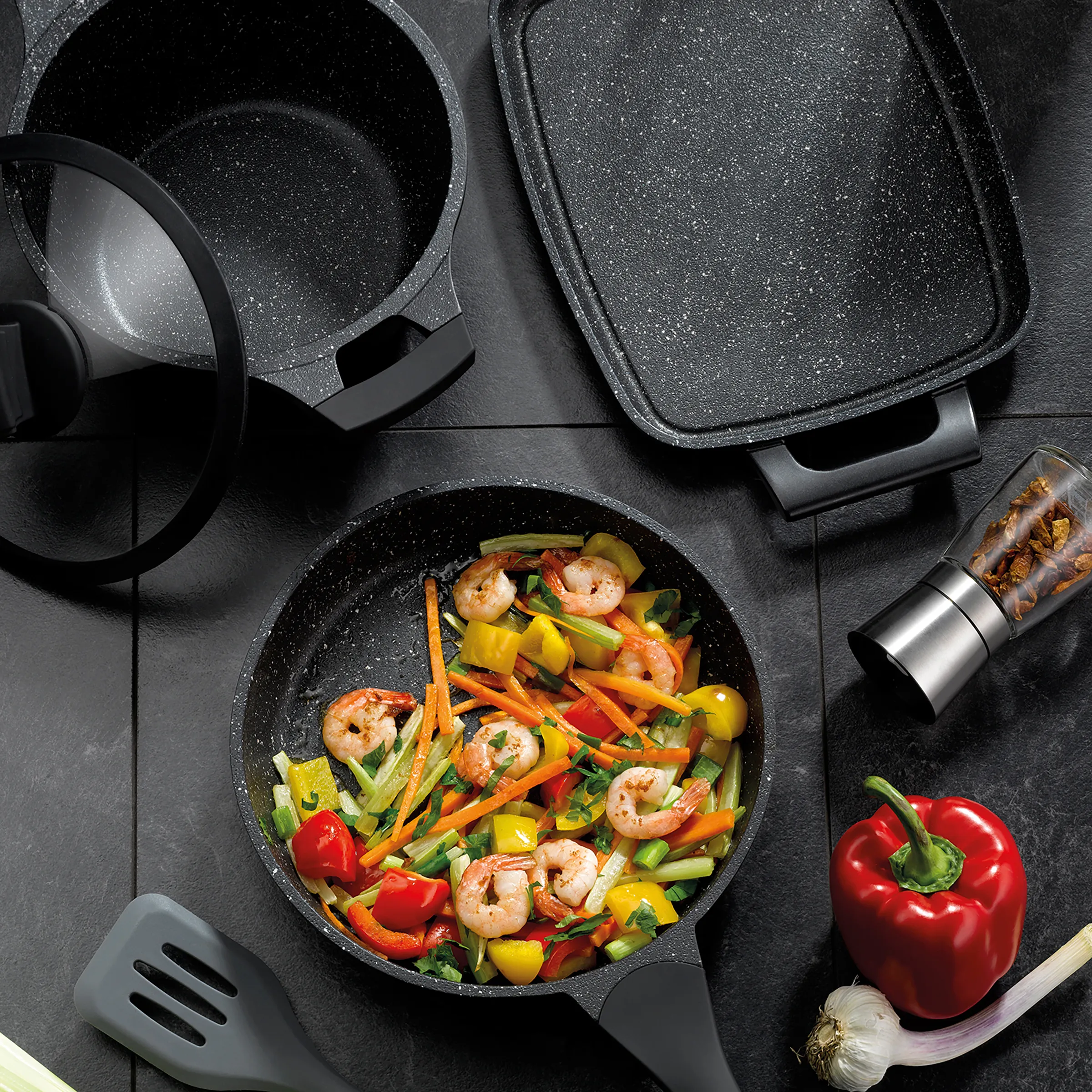 Granitbeschichtetes Kochgeschirr-Set mit Wok, Pfanne und Garnelen-Gemüse-Pfanne auf dunkler Oberfläche