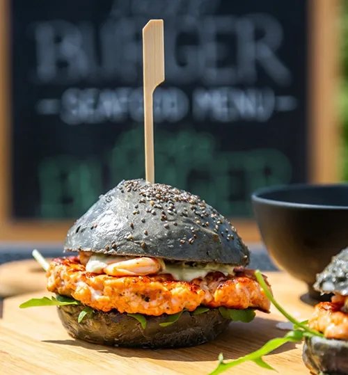 Premium Burger - Gourmet Burger Rezept Gourmet-Burger mit schwarzem Sesambrötchen, würzigem Patty und grünem Mikrogrün auf Holzbrett