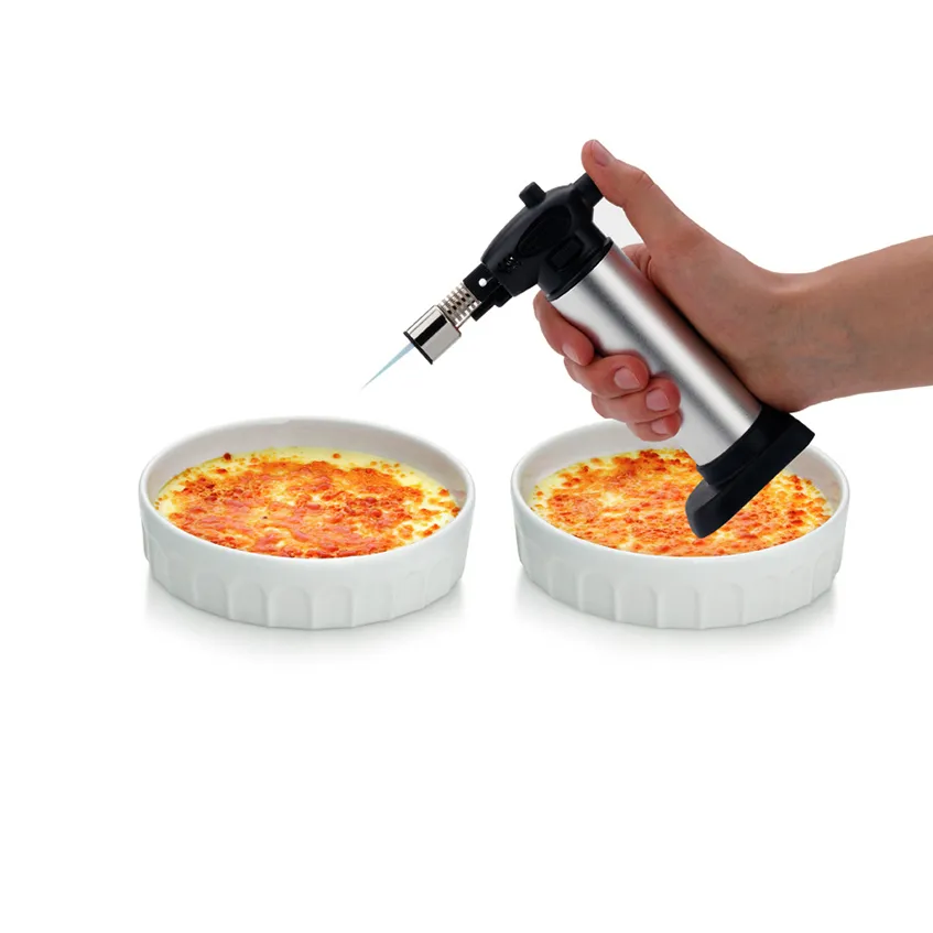 Küchenprofi Flambierbrenner für Crème Brûlée Hand hält Küchenprofi-Flambierbrenner über Crème Brûlée in weißer Schale