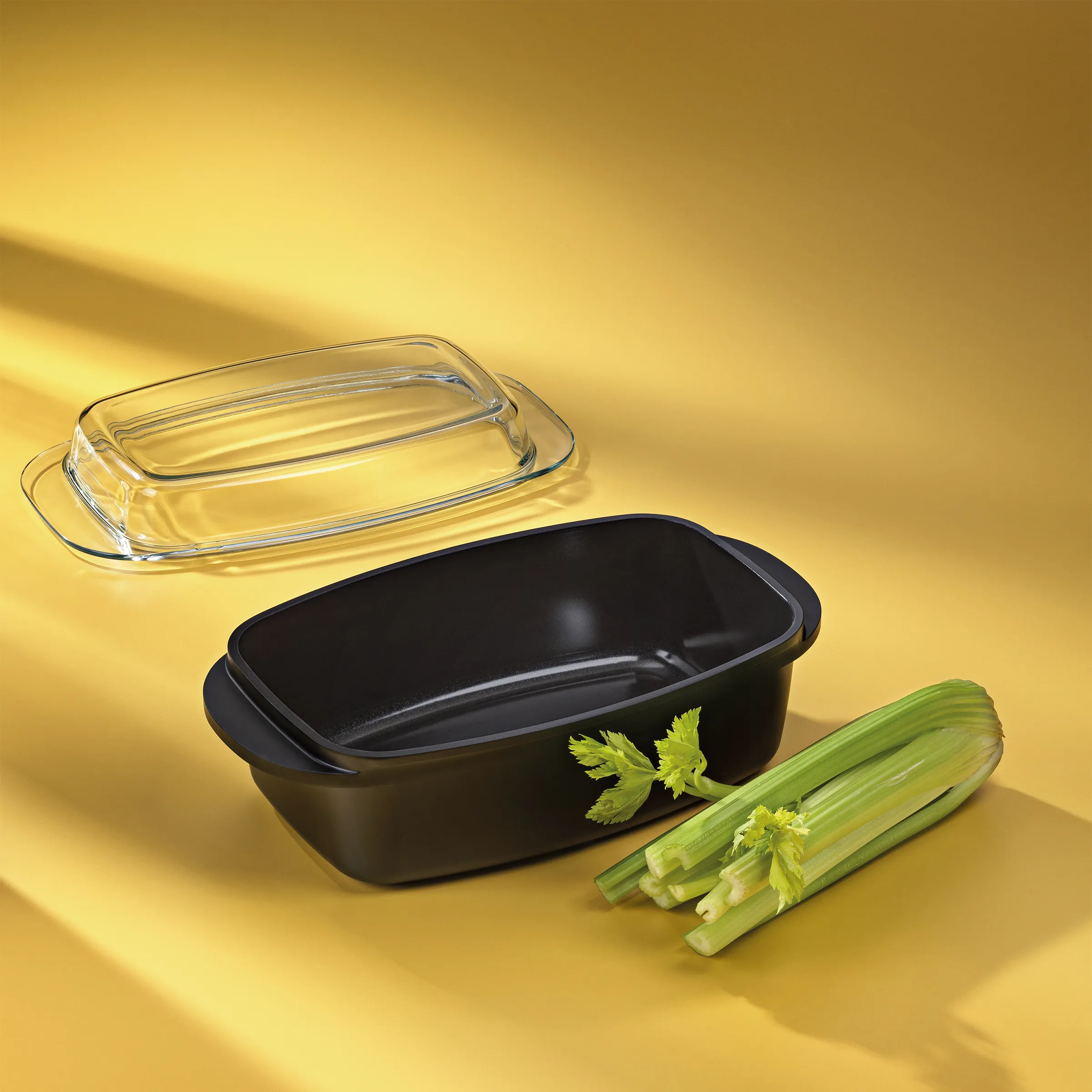 Auflaufform schwarz mit Glasdeckel – Backform Set Schwarze Auflaufform mit Glasdeckel und frischen Stangensellerie auf gelbem Hintergrund