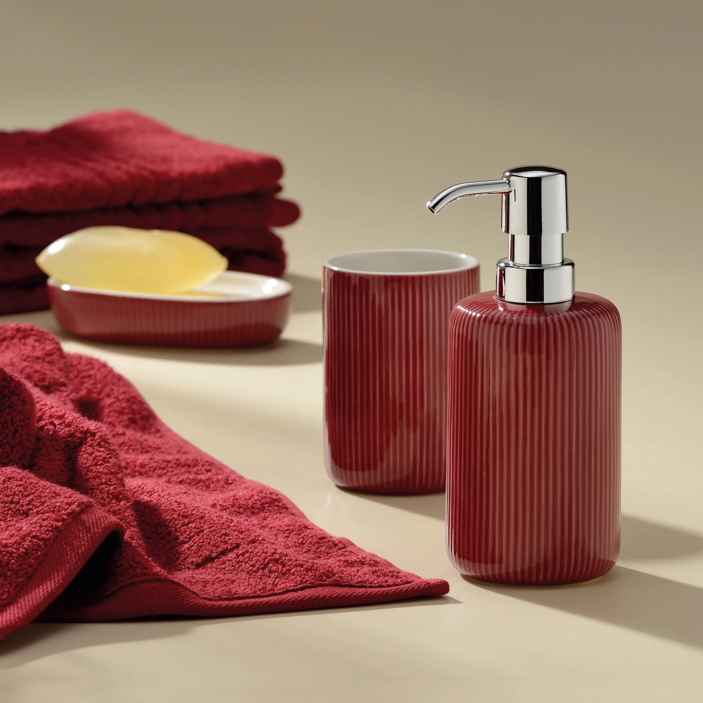 Badezimmer Accessoires Set Rot - Seifenspender & Handtücher Badezimmer-Set mit rotem Seifenspender, Zahnbürstenbecher, Seifenschale und Handtüchern auf beigem Hintergrund