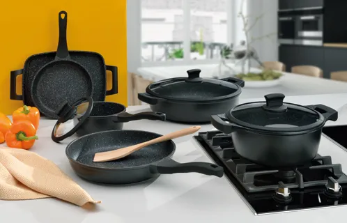 Schwarzes antihaftbeschichtetes Kochgeschirr-Set mit Pfannen, Töpfen und Deckeln auf Gaskochfeld und Holzbrett