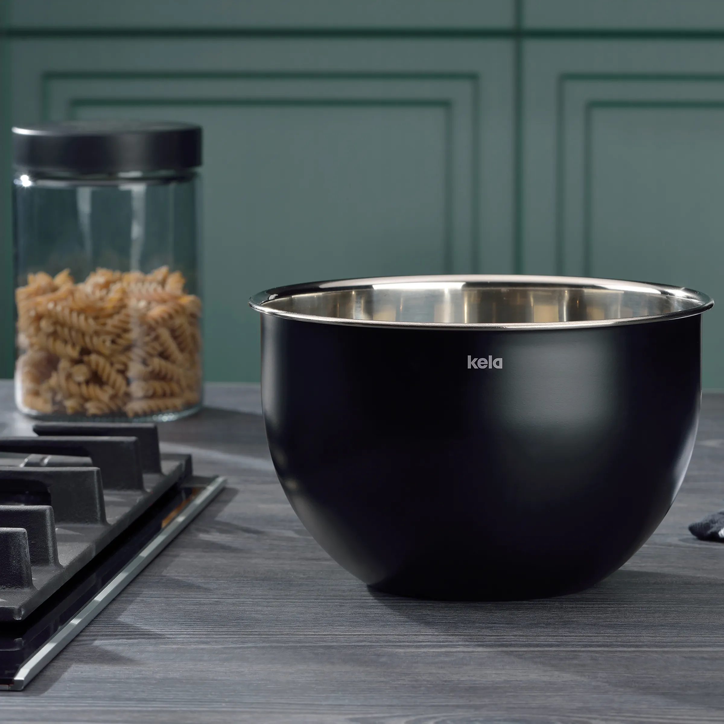Kela Rührschüssel schwarz mit Edelstahlrand - Küchenschüssel für Teig und Zubereitung Schwarze Kela Rührschüssel mit Edelstahlrand auf Arbeitsplatte, daneben Vorratsglas mit Pasta