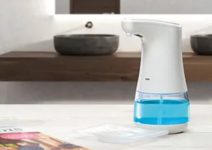 Automatischer Seifenspender aus Kunststoff mit blauer Flüssigkeit auf Badezimmer-Waschtisch neben schwarzer Schüssel