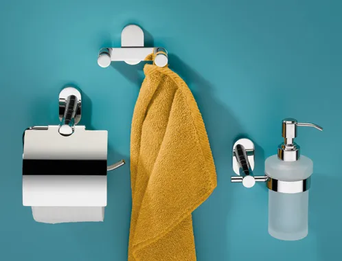 Modernes Badezimmer-Set mit Chromarmaturen: Toilettenpapierhalter, Handtuchstange mit gelbem Handtuch und Seifenspender an türkisblauer Wand