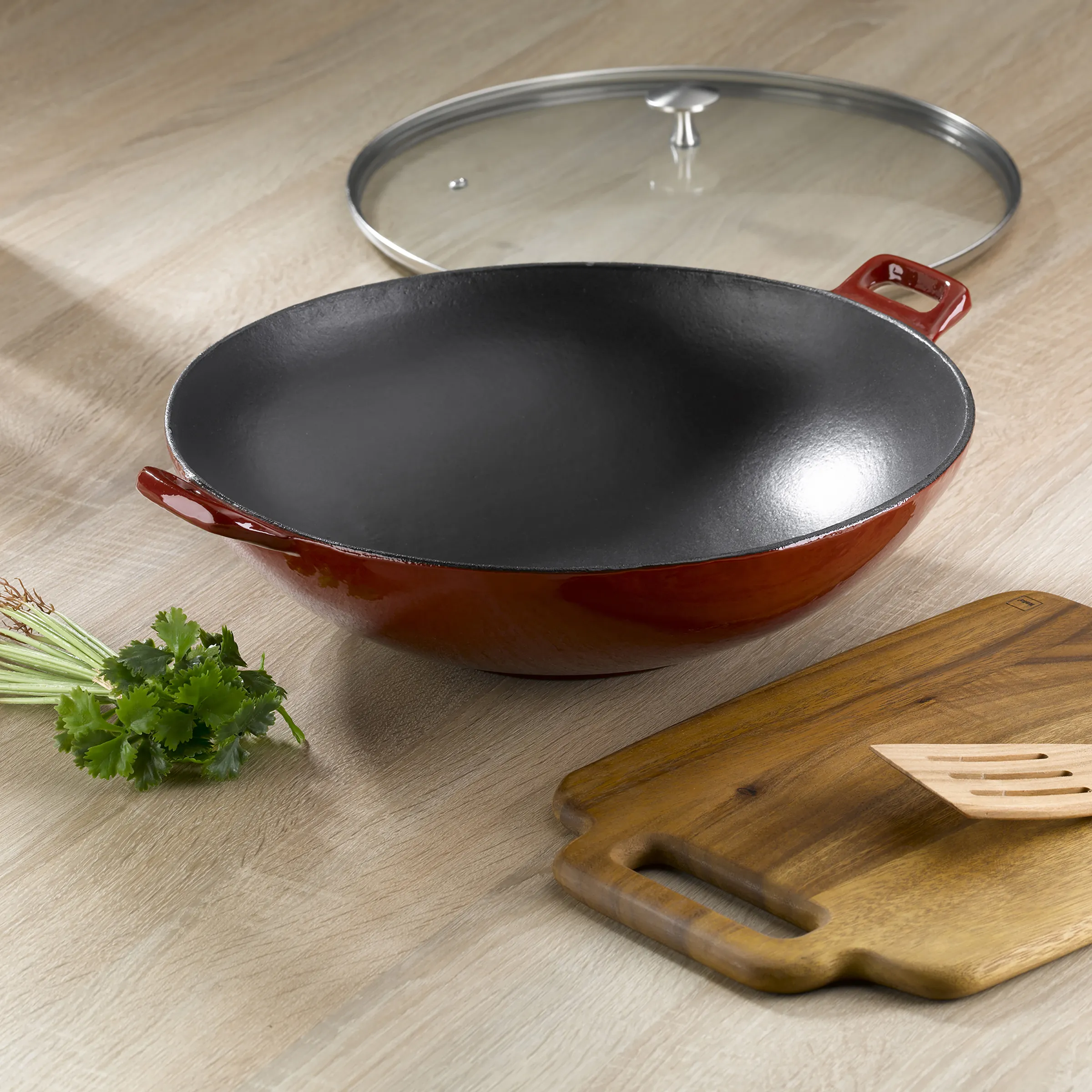 Wok-Pfanne mit Antihaftbeschichtung und Glasdeckel - Antihaft Wok rot Rote Wok-Pfanne mit Antihaftbeschichtung, Glasdeckel und zwei Griffen auf Holzunterlage mit Koriander