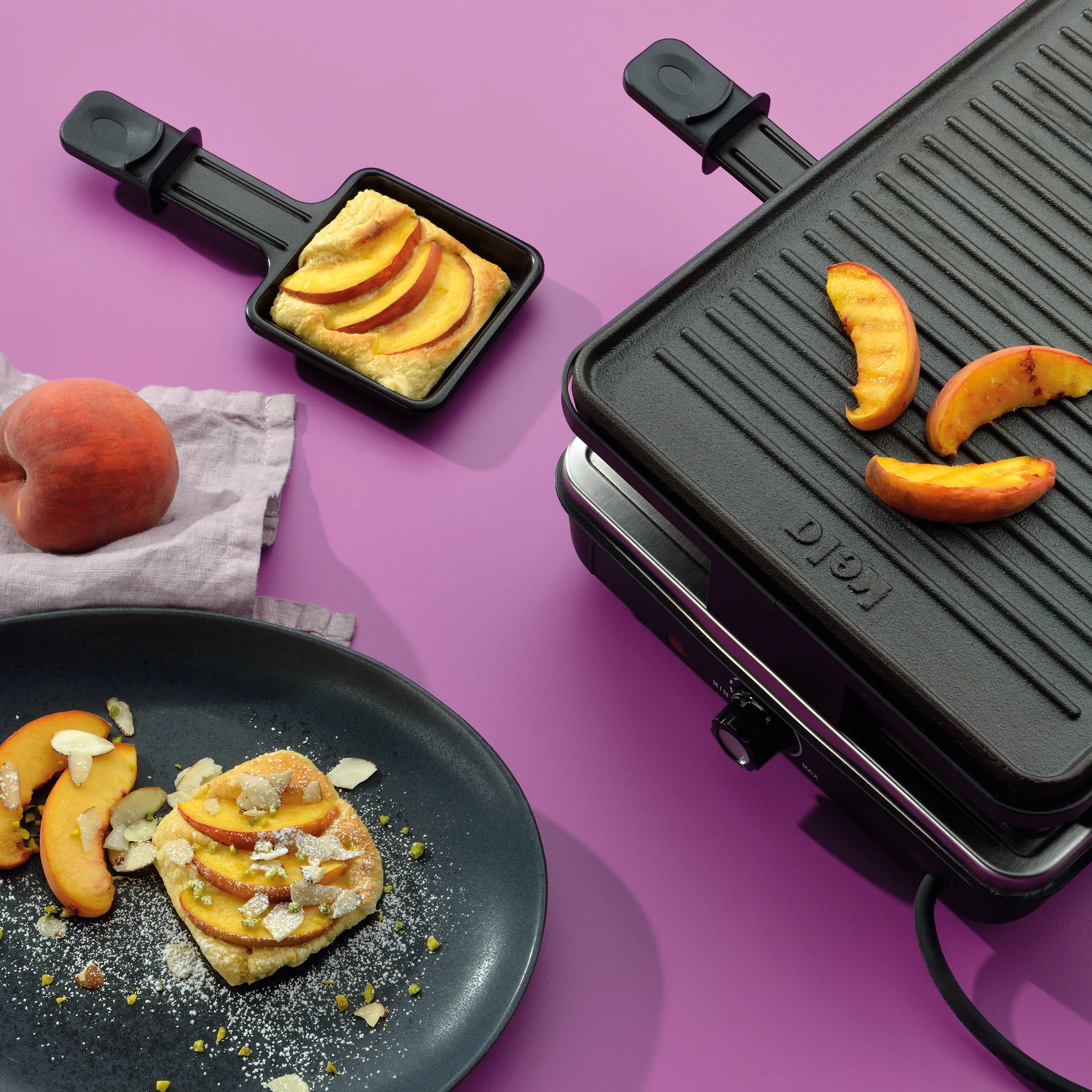 Raclette-Grill mit gegrillten Pfirsichscheiben und Pancakes mit Pfirsich-Topping auf rosa Hintergrund