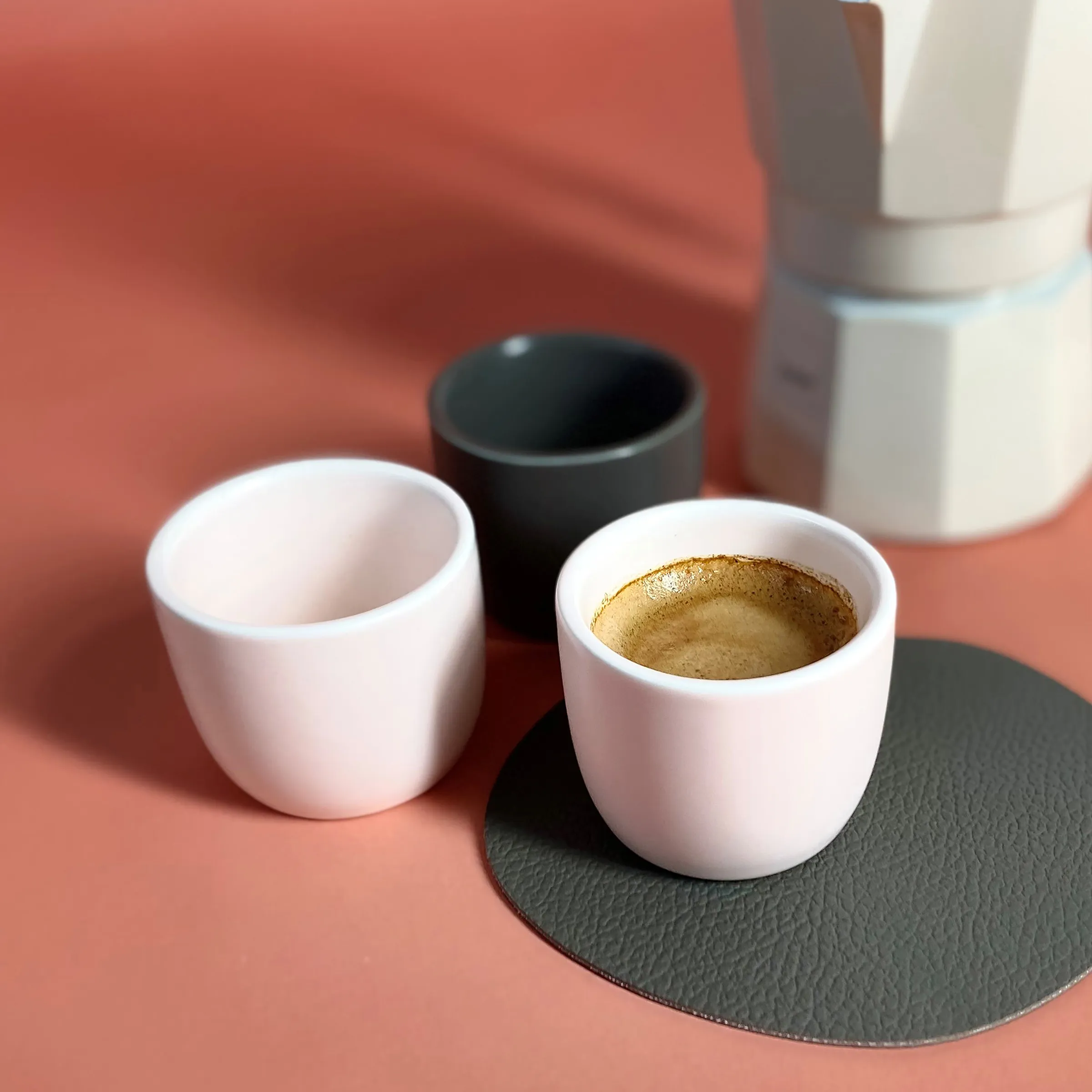 Moderne Espressotassen Set - Weiße Porzellan Kaffeebecher auf schwarzem Untersetzer Zwei weiße Porzellanbecher mit Espresso auf schwarzem Untersetzer, umgeben von weiteren Tassen