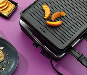 Doppel-Kontaktgrill mit schwarzen Platten auf violettem Hintergrund, gekochte Hähnchenschenkel und Gemüse auf der Oberfläche