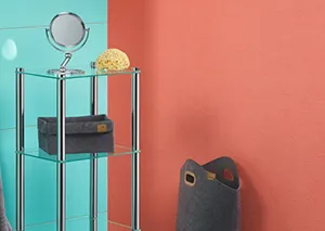 Modernes Badezimmer mit türkisem Regal, Spiegel, Kosmetikprodukten und schwarzem Behälter vor korallenfarbener Wand.