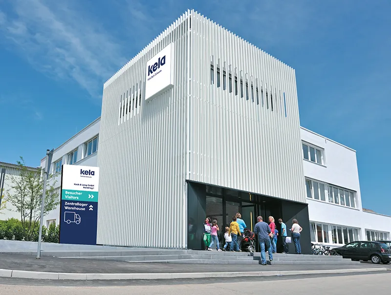 kela Unternehmensgebäude - Moderne Architektur Firmenstandort Modernes kela Gebäude mit charakteristischer vertikaler Rippenfassade und Eingangsbereich mit Besuchern