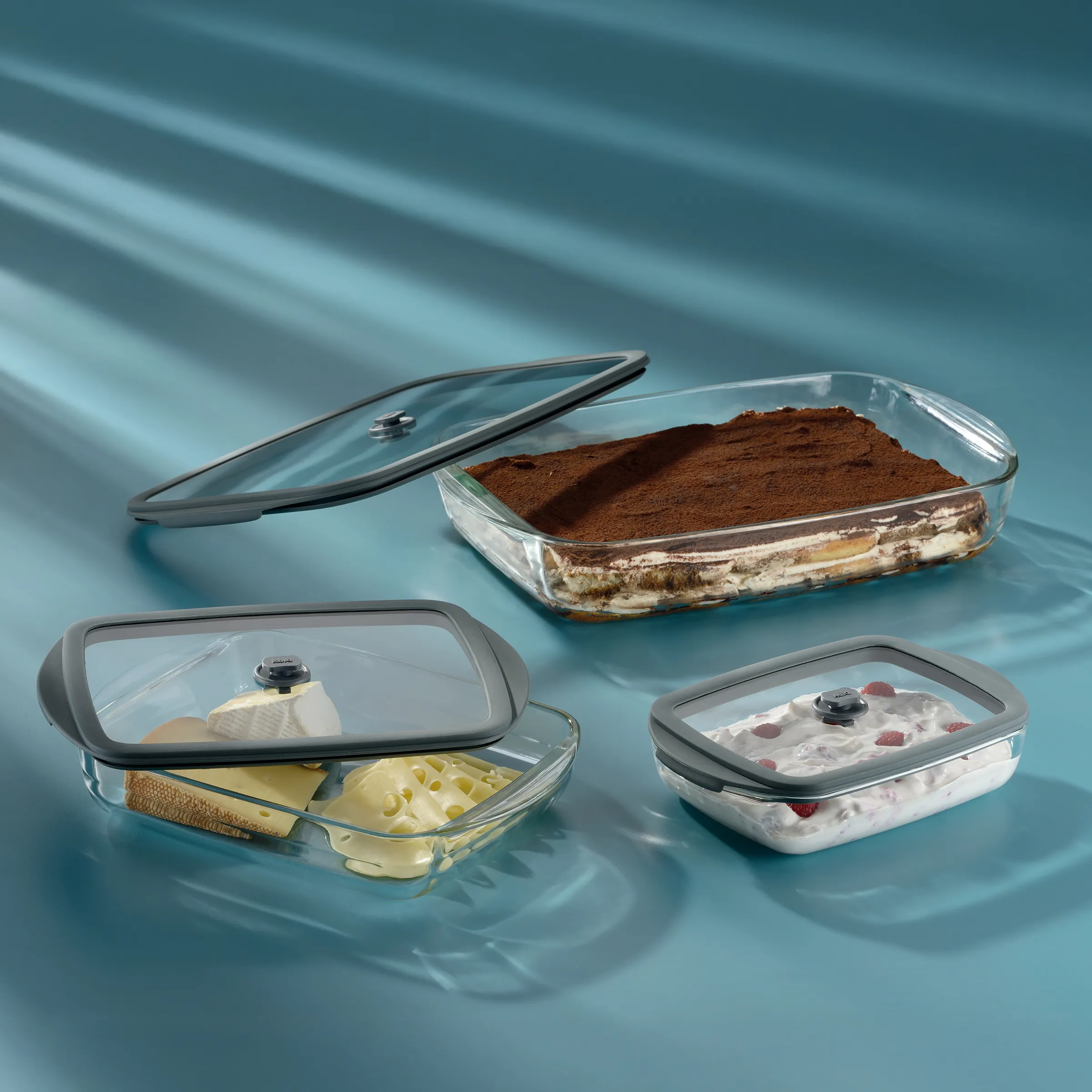 Vier Glasschüsseln mit Deckel auf blauem Untergrund: Tiramisu, Butter mit Käse, Dessert mit Beeren und Kakao-Pulver.