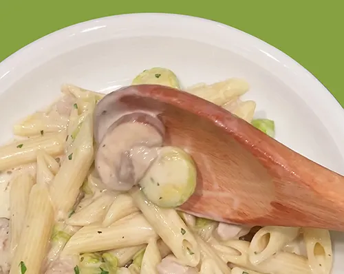 Penne Pasta mit Kräutern - Italienische Nudeln auf weißem Teller Penne-Nudeln mit Kräutern auf weißem Teller, serviert mit einem Holzlöffel auf grünem Hintergrund