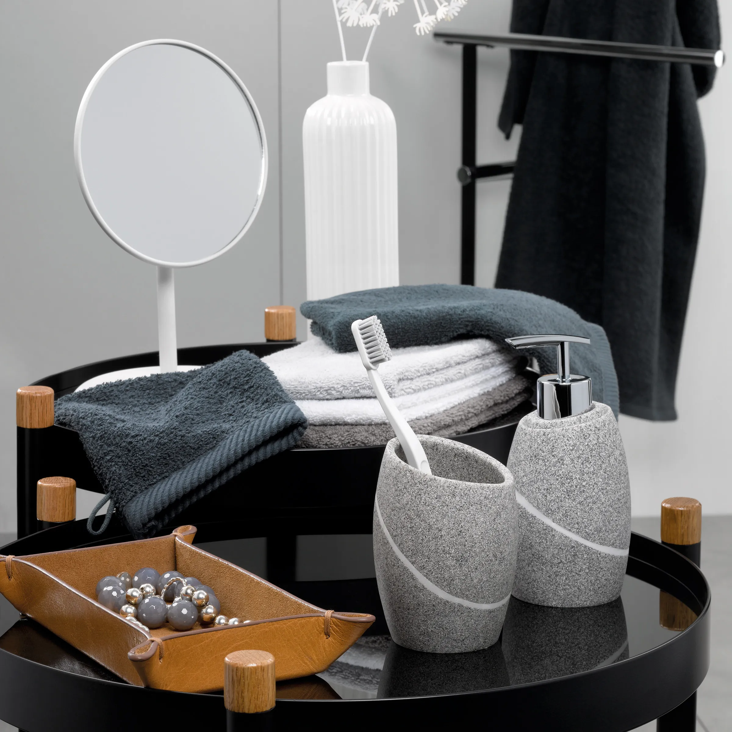Badezimmer-Accessoires Set grau mit Seifenspender und Zahnputzbecher Modernes Badezimmer-Set mit grauem Zahnputzbecher, Seifenspender, Handtüchern und Dekoration auf schwarzem Tablett
