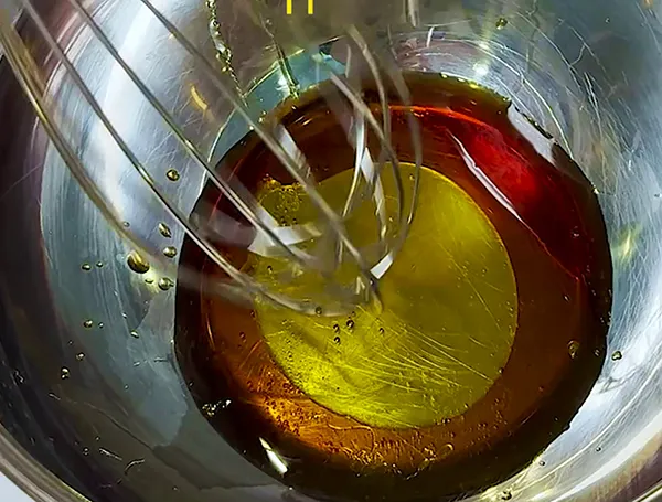 Industrieller Mischer für Lebensmittelproduktion - Öl und Flüssigkeiten vermischen Rührgerät mischt gelbe und rote Flüssigkeit in Edelstahlschüssel bei der Lebensmittelherstellung