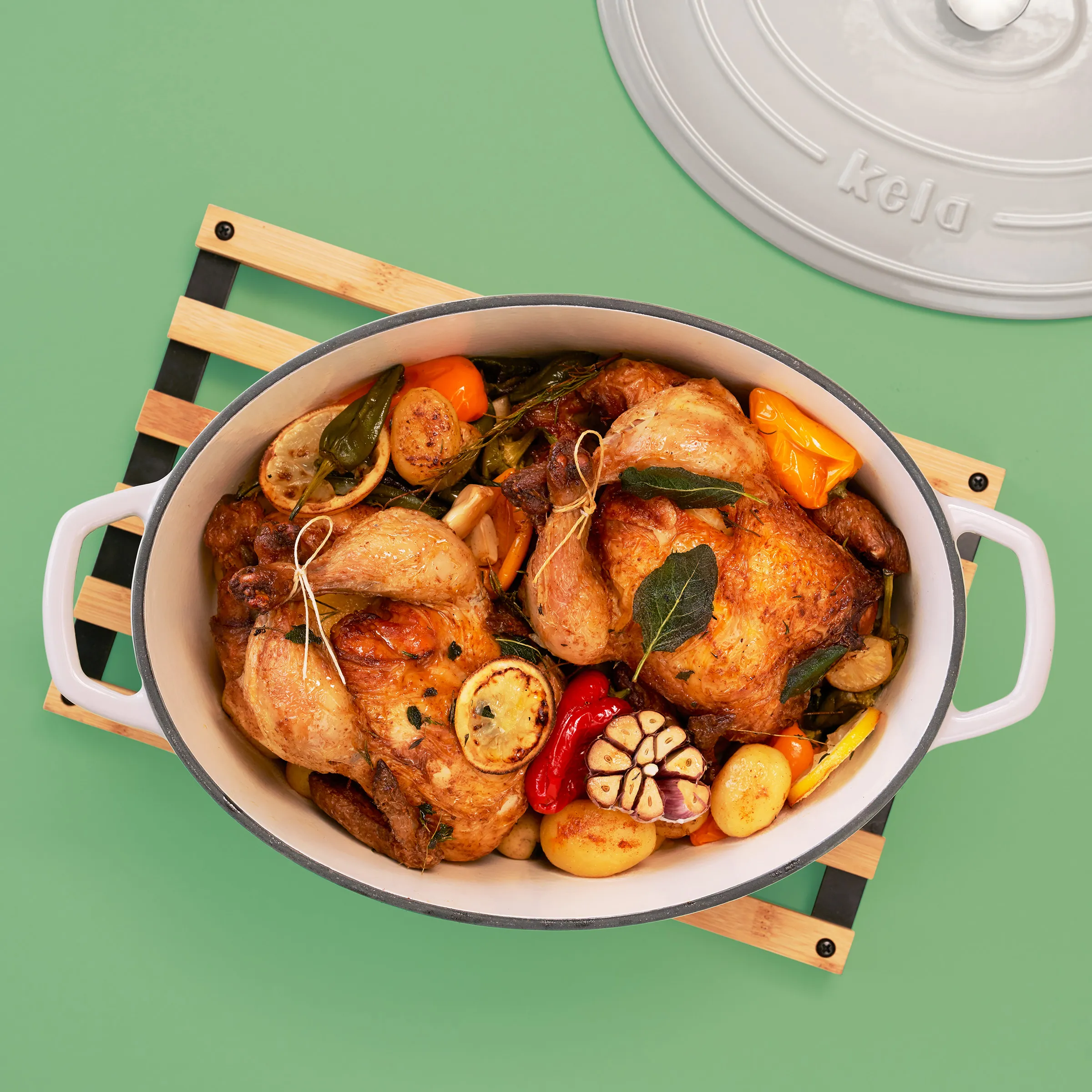 Gebratenes Hähnchen mit Gemüse im Schmortopf - Ofengericht Rezept Gebratenes Hähnchen mit Gemüse und Kartoffeln in weißem Schmortopf auf Holzbrett, grüner Hintergrund