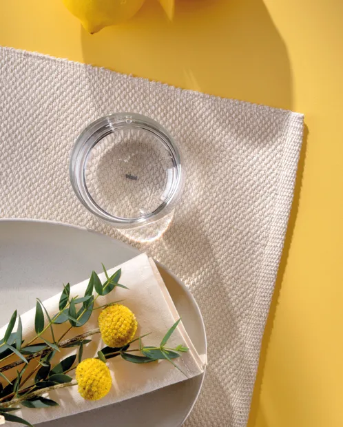 Minimalistische Produktfotografie mit Glasschale und Blumendeko Flaches Produktfoto mit gelbem Hintergrund: Glasschale auf Leinenstoff, daneben gelbe Blüten und grüne Blätter auf weißem Teller