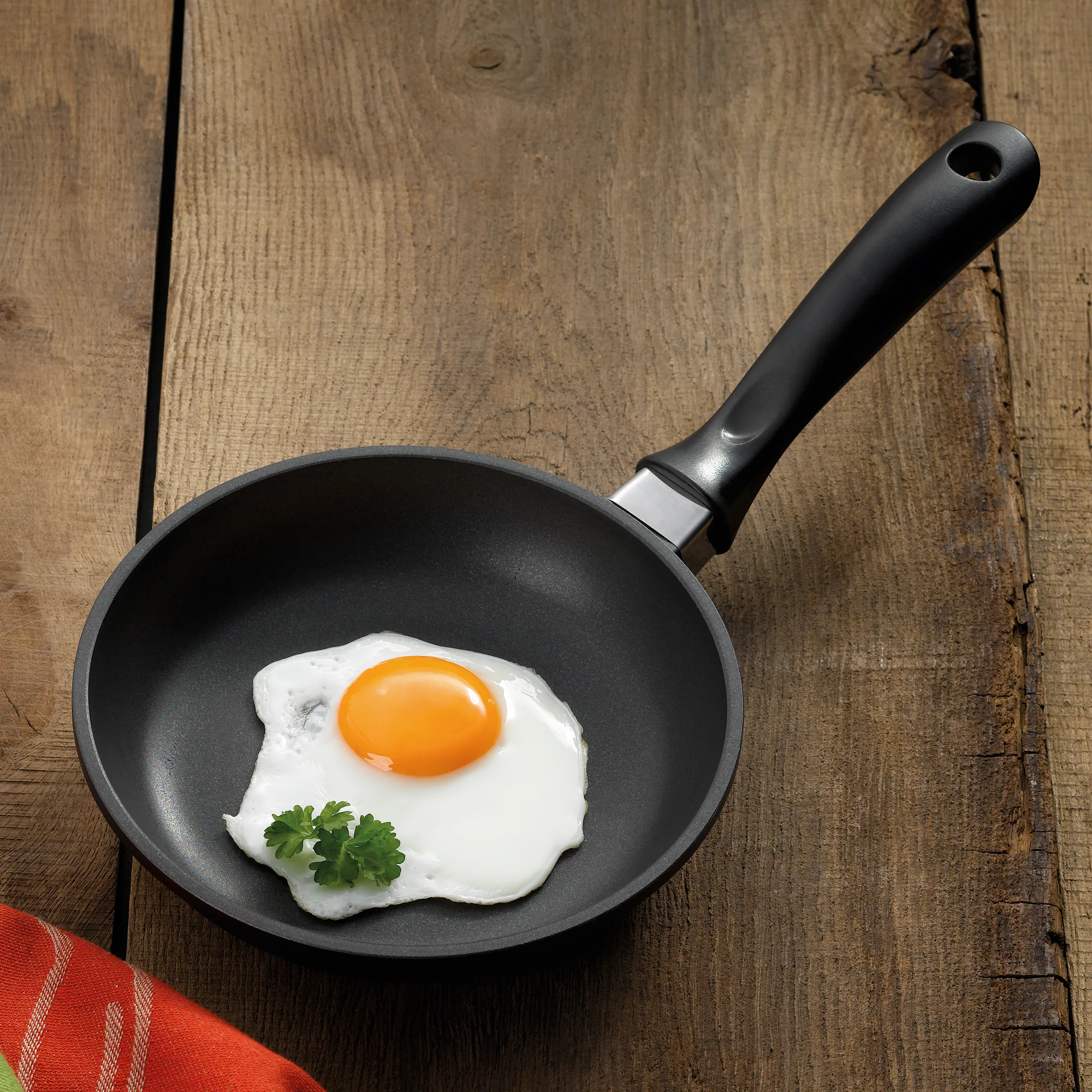 Antihaft-Bratpfanne mit Spiegelei – Non-Stick Pfanne für die Küche Schwarze Bratpfanne mit Spiegelei und Petersilie auf rustikalem Holztisch