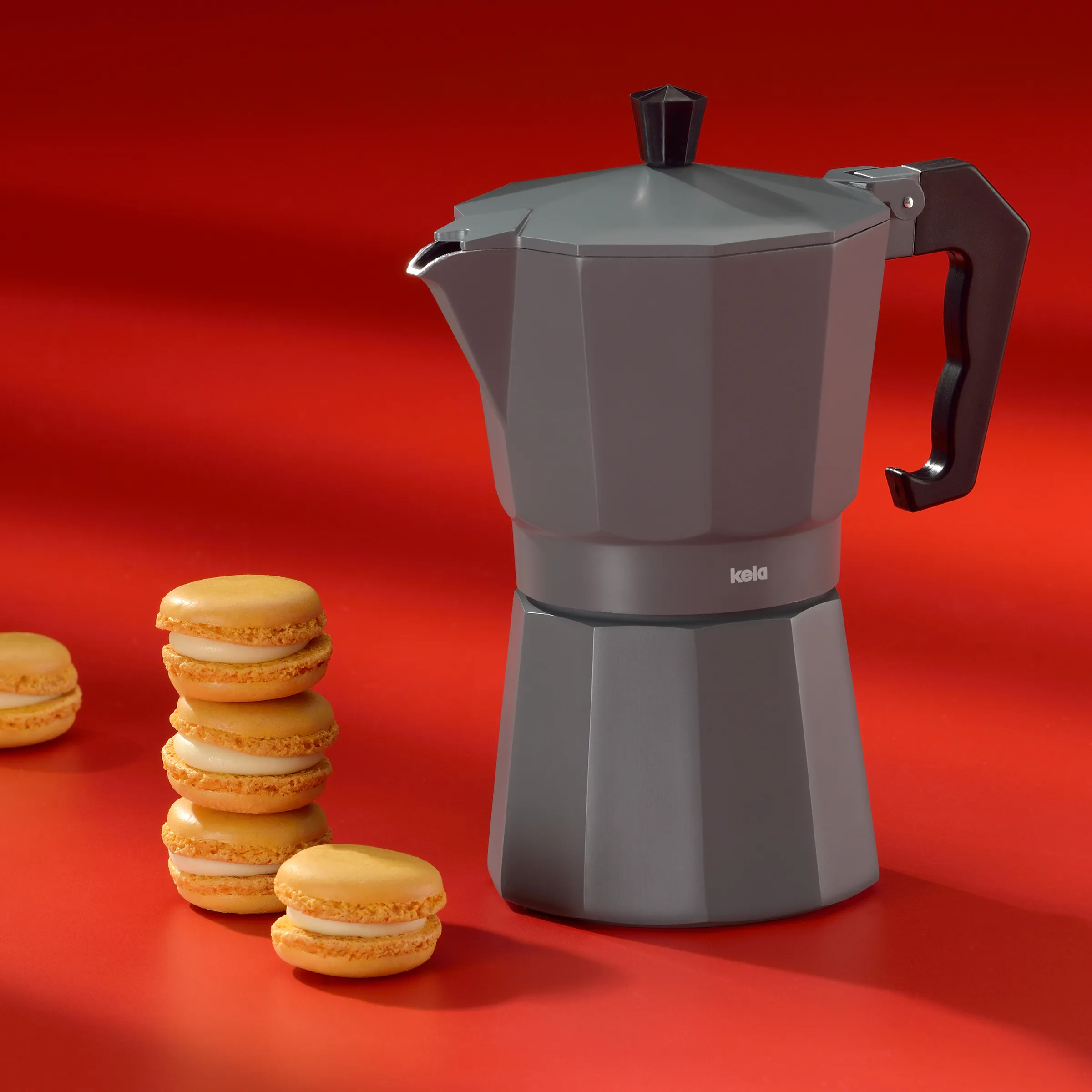 Kela Espressokanne grau mit Macarons – Kaffeezubereitung Stillleben Graue Espressokanne von kela mit orangefarbenen Macarons auf rotem Hintergrund
