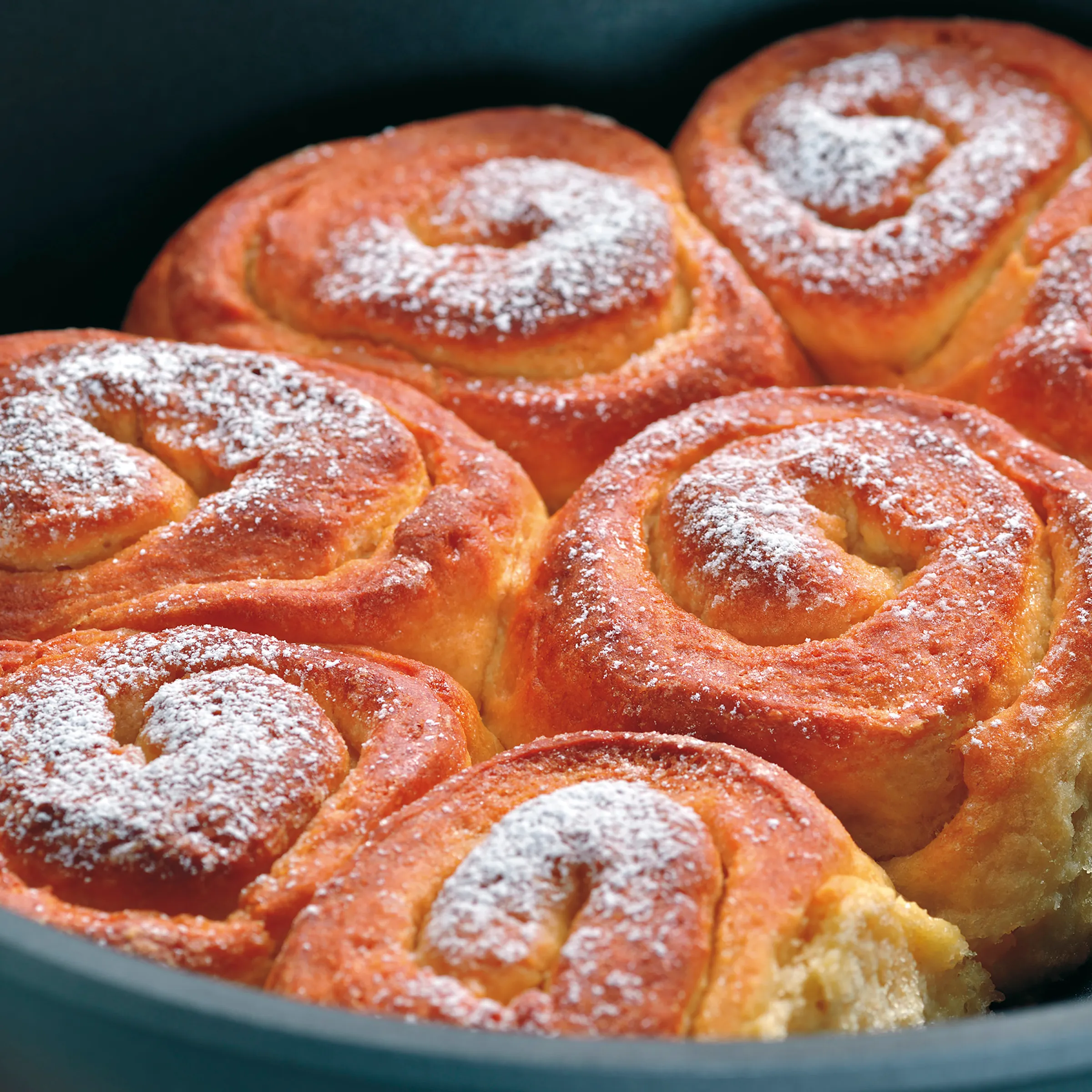 Zimtschnecken Rezept - köstliche Backware mit Zucker Frische Zimtschnecken mit Puderzucker bestreut in einer grünen Schüssel, goldbraun gebacken