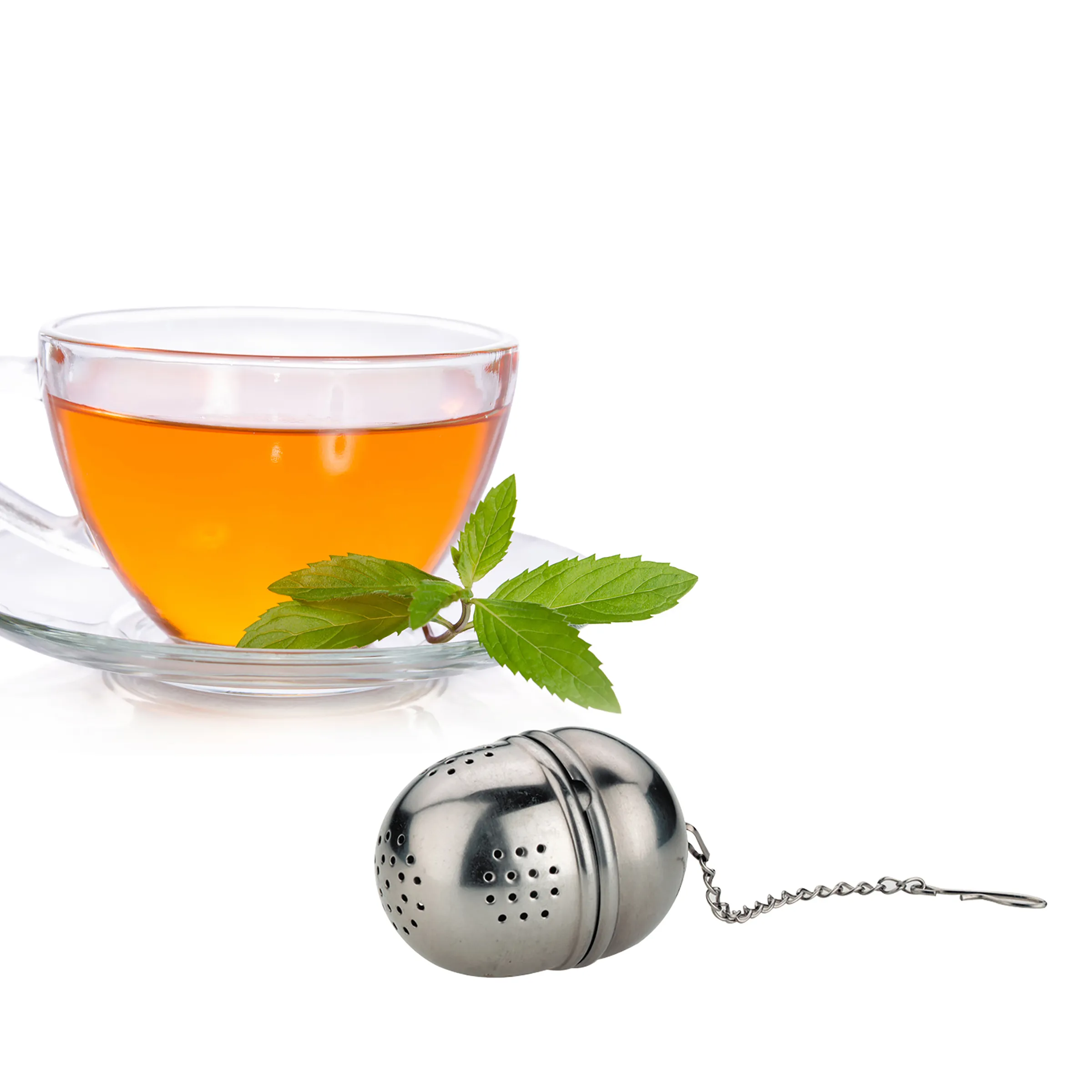 Glastasse mit goldenem Tee, frischen Minzblättern und einem Edelstahl-Tee-Ei mit Kette auf weißem Untergrund.