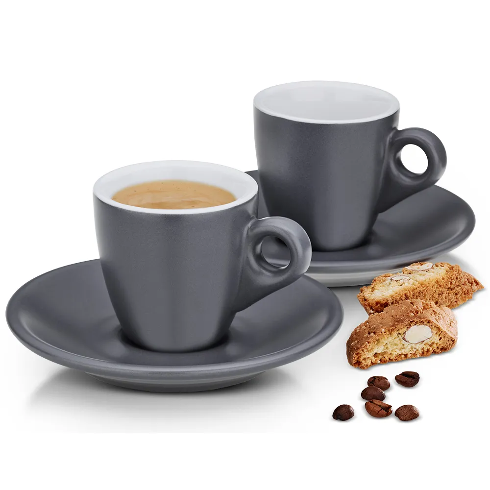 Zwei graue Espressotassen mit Untertassen, eine gefüllt mit Kaffee, daneben Biscotti und Kaffeebohnen auf weißem Hintergrund.