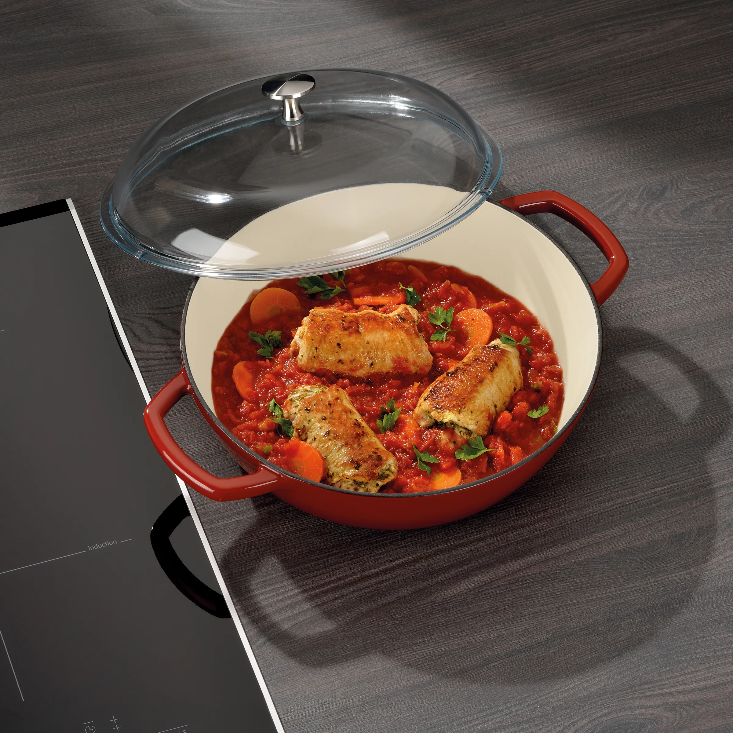 Induktionsgeeigneter Bräter mit Glasdeckel - Hähnchen in Tomatensauce Roter Bräter mit Glasdeckel und Hähnchen in Tomatensauce auf Induktionskochfeld