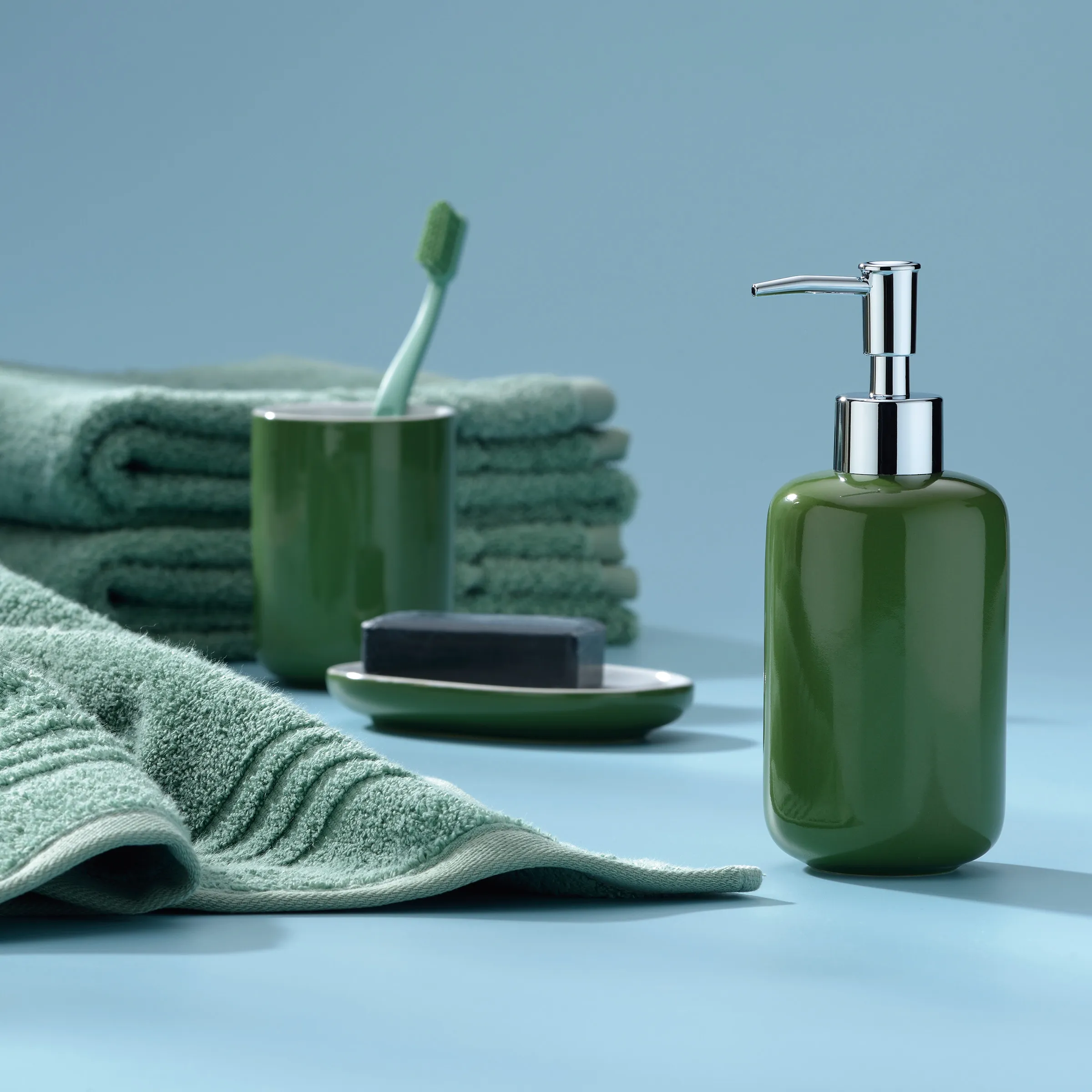 Grüne Badezimmeraccessoires auf blauem Hintergrund: Handtücher, Zahnbürste, Seife und Pumpenflasche