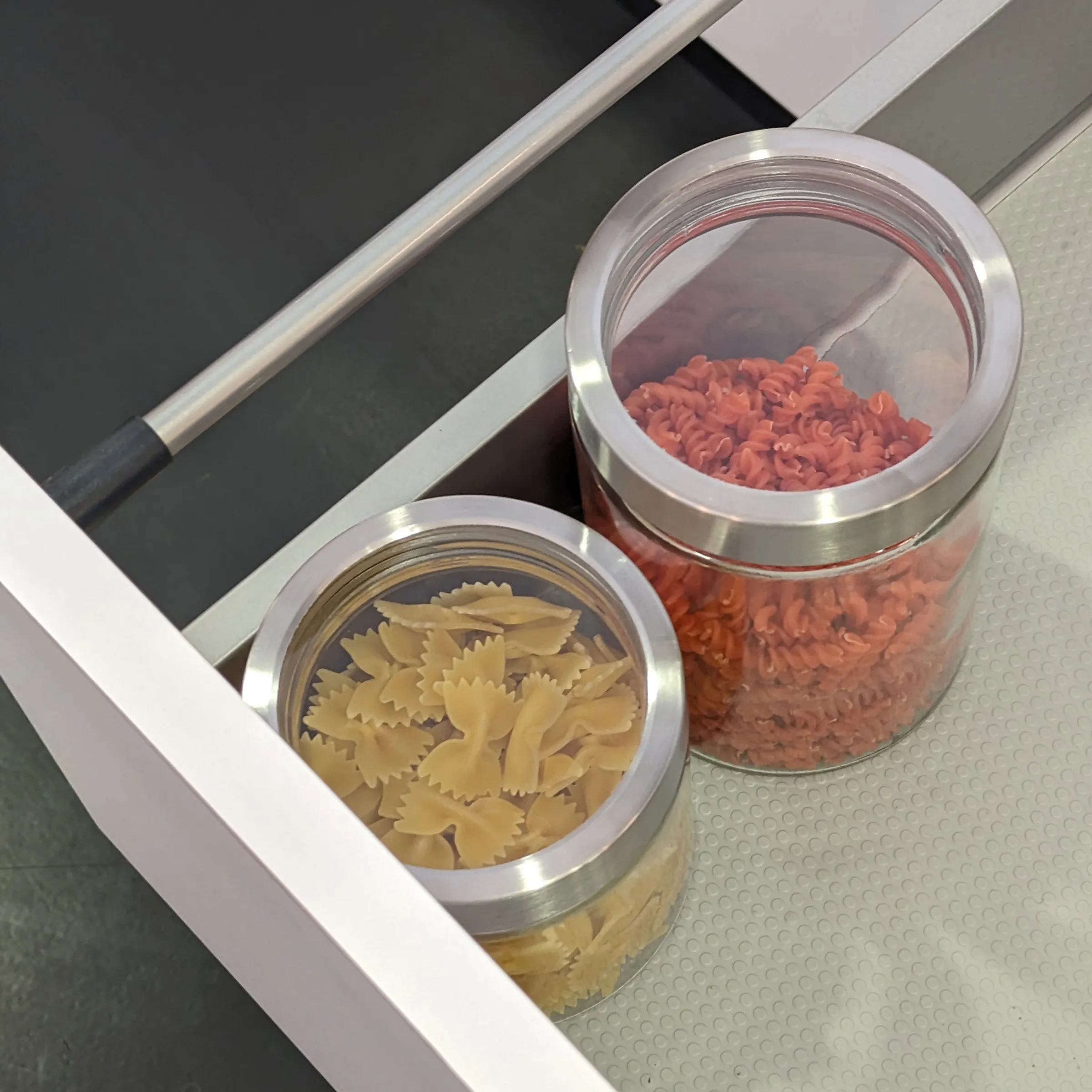 Zwei Vorratsgläser mit Nudeln in Küchenschublade - gelbe Farfalle und rote Fusilli in transparenten Behältern