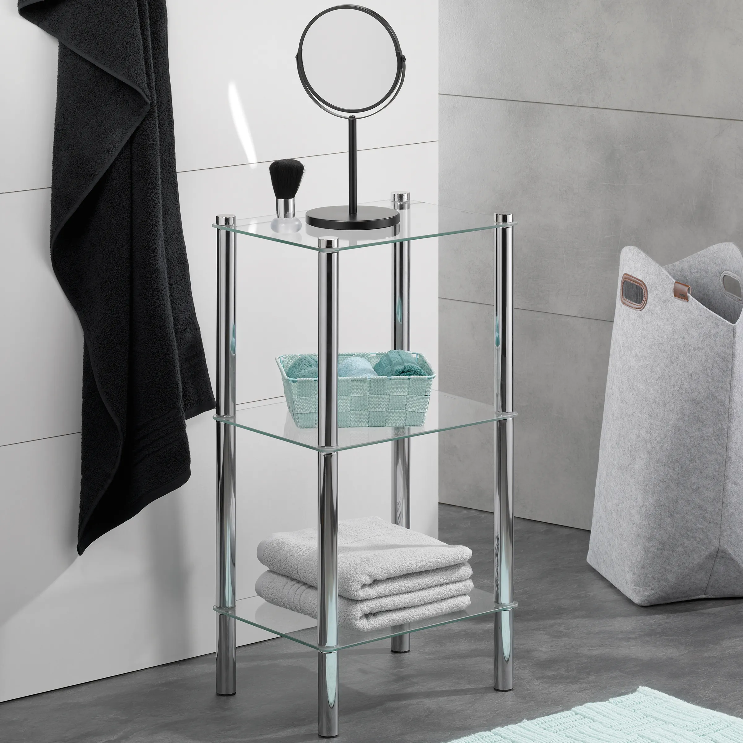 Modernes Bad-Regal aus Glas und Edelstahl mit drei Ebenen, dekorativen Accessoires und Handtüchern.