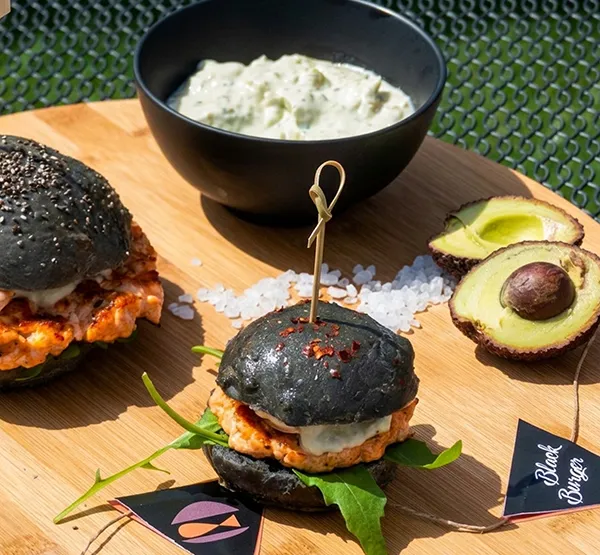 Schwarze Burger mit Avocado - Gourmet Fast Food Schwarze Burger mit Avocado, Sauce und grünem Salat auf Holzbrett mit Dip-Schale