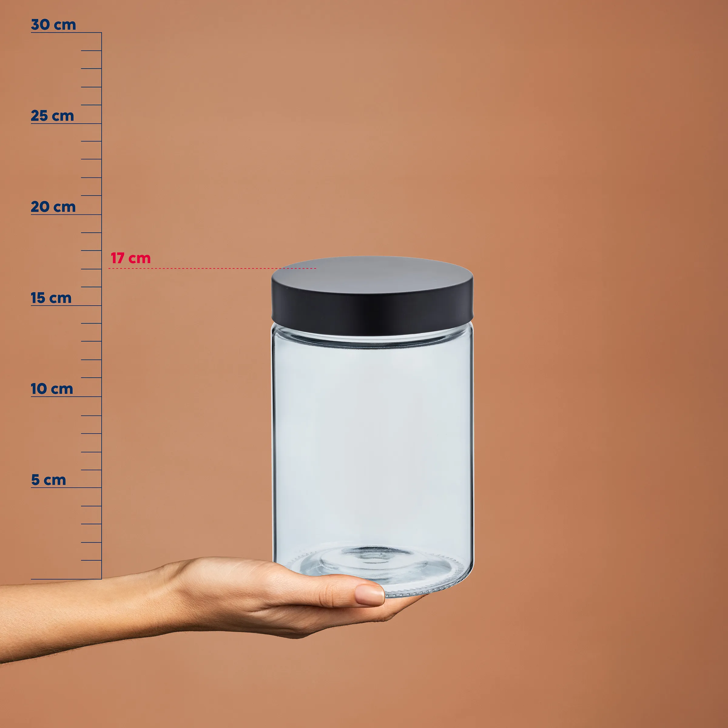 Glasbehälter mit Deckel - Vorratsglas für Lagerung Transparentes Glasgefäß mit schwarzem Deckel auf einer Hand, neben einer Messskala mit Markierungen bis 30 cm. Durchmesser etwa 17 cm.