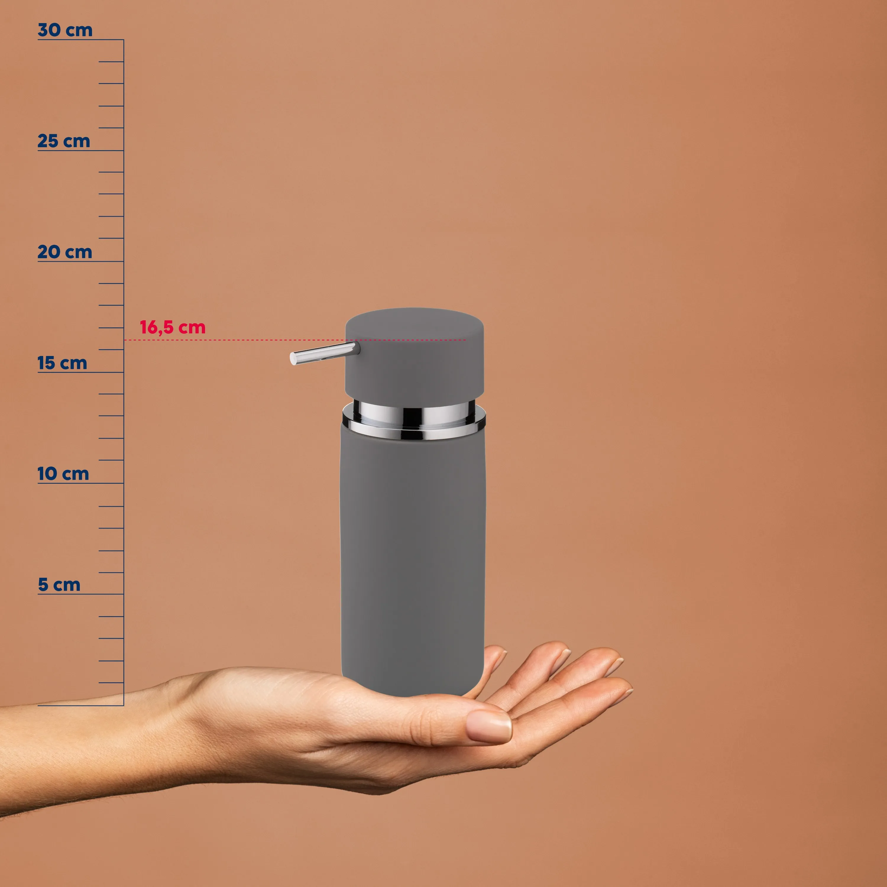 Distributeur de savon gris avec bouton-poussoir argenté reposant sur une main ouverte, avec échelle de référence de taille